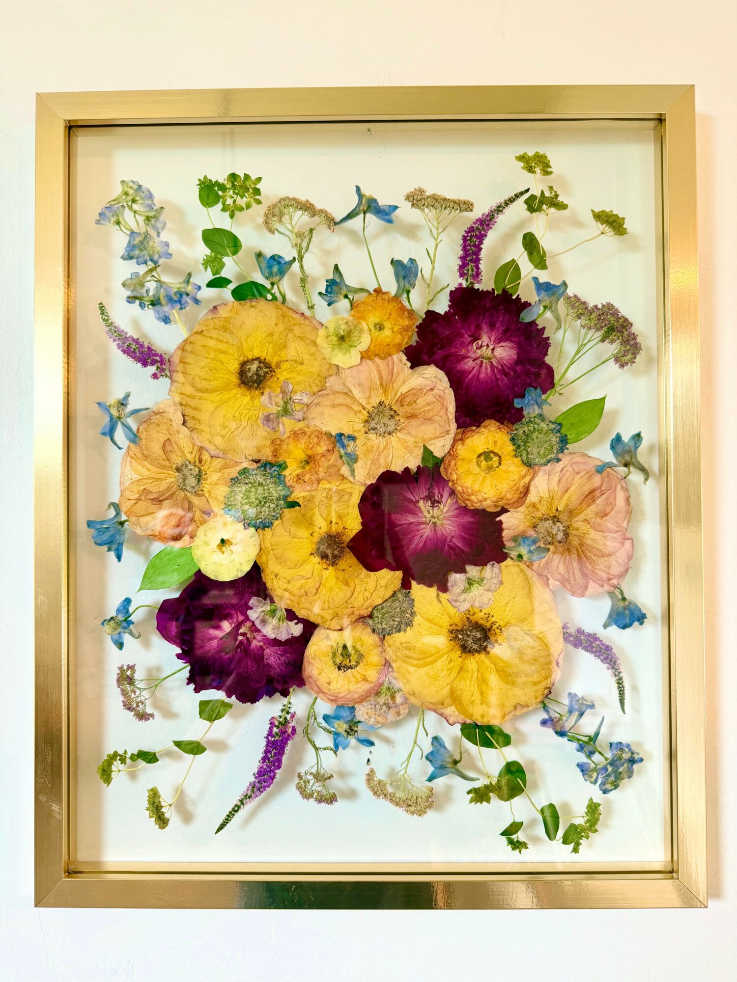 Framed floral artwork with yellow, purple, and pink flowers, and green leaves, arranged in a colorful pattern.