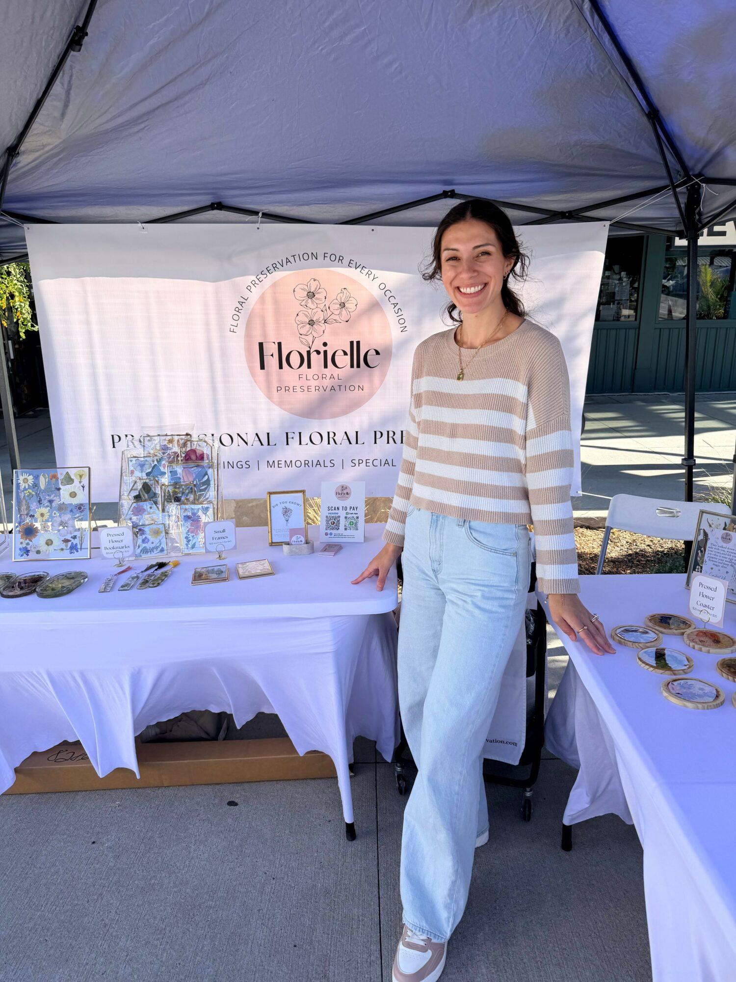 Woman standing next to a table with products and a banner, smiling, indoors, with a white tablecloth.