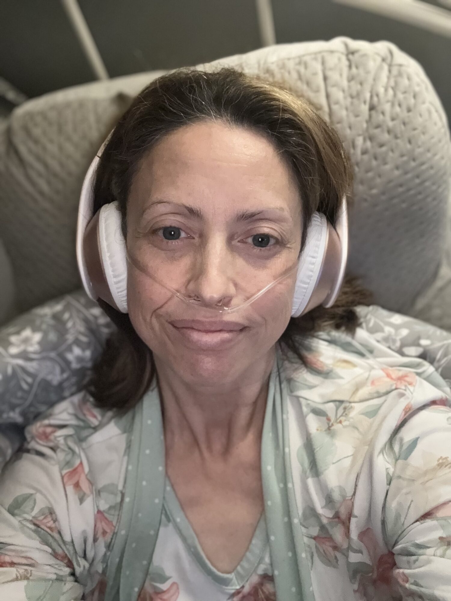 Woman with headphones lying on a bed, looking at the camera, with a neutral expression.