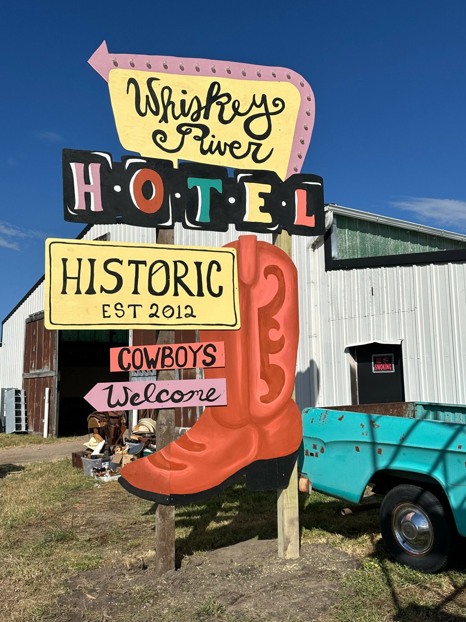 Sign with colorful letters and a large orange sculpture in front, with a building and blue sky in the background.