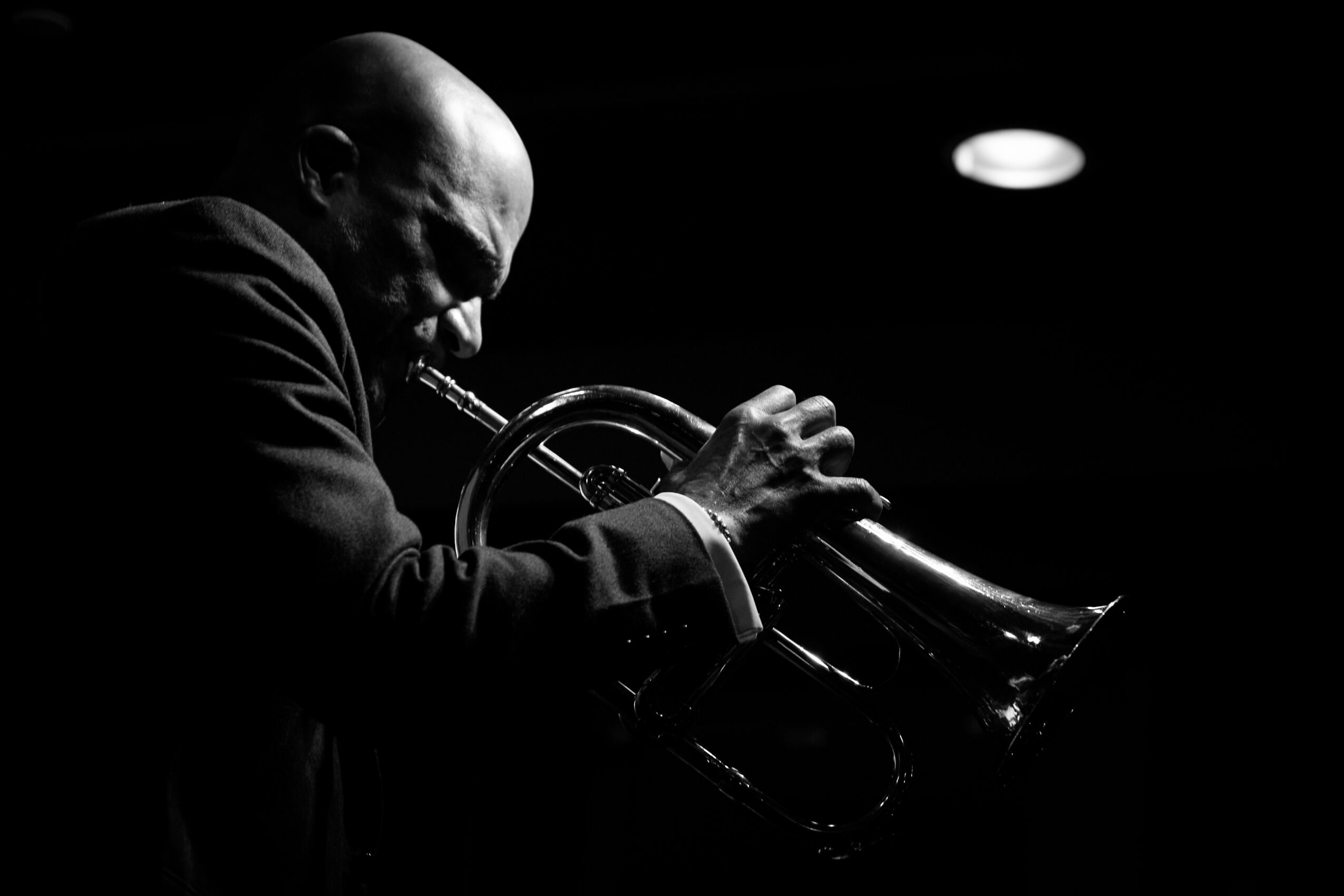 A person playing a trumpet in a dark setting, with a spotlight highlighting their face and instrument.