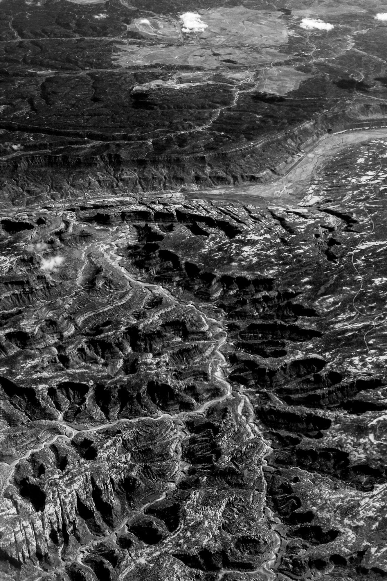 Aerial view of rugged, rocky terrain with deep crevices and layered formations, in black and white.
