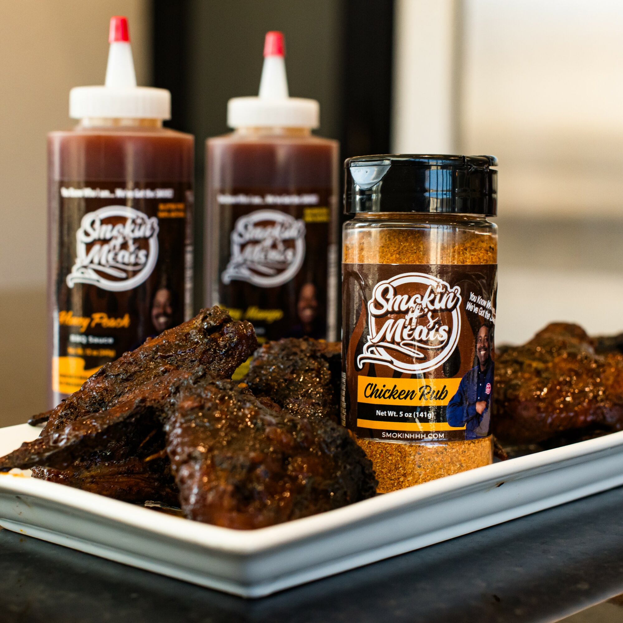 Barbecue ribs with sauce, two bottles of barbecue sauce, and a jar of chicken rub on a white tray.