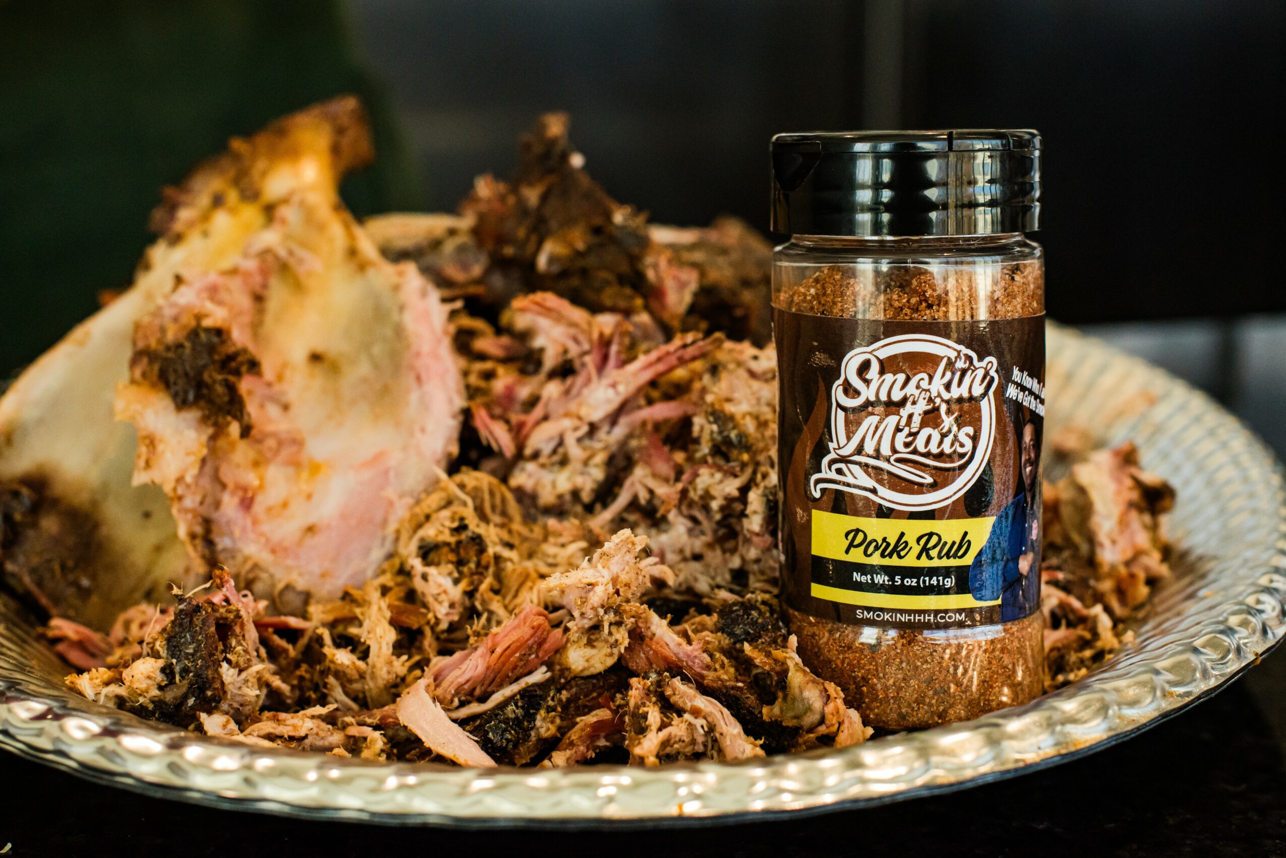 A plate with shredded smoked pork and a jar of pork rub seasoning labeled 