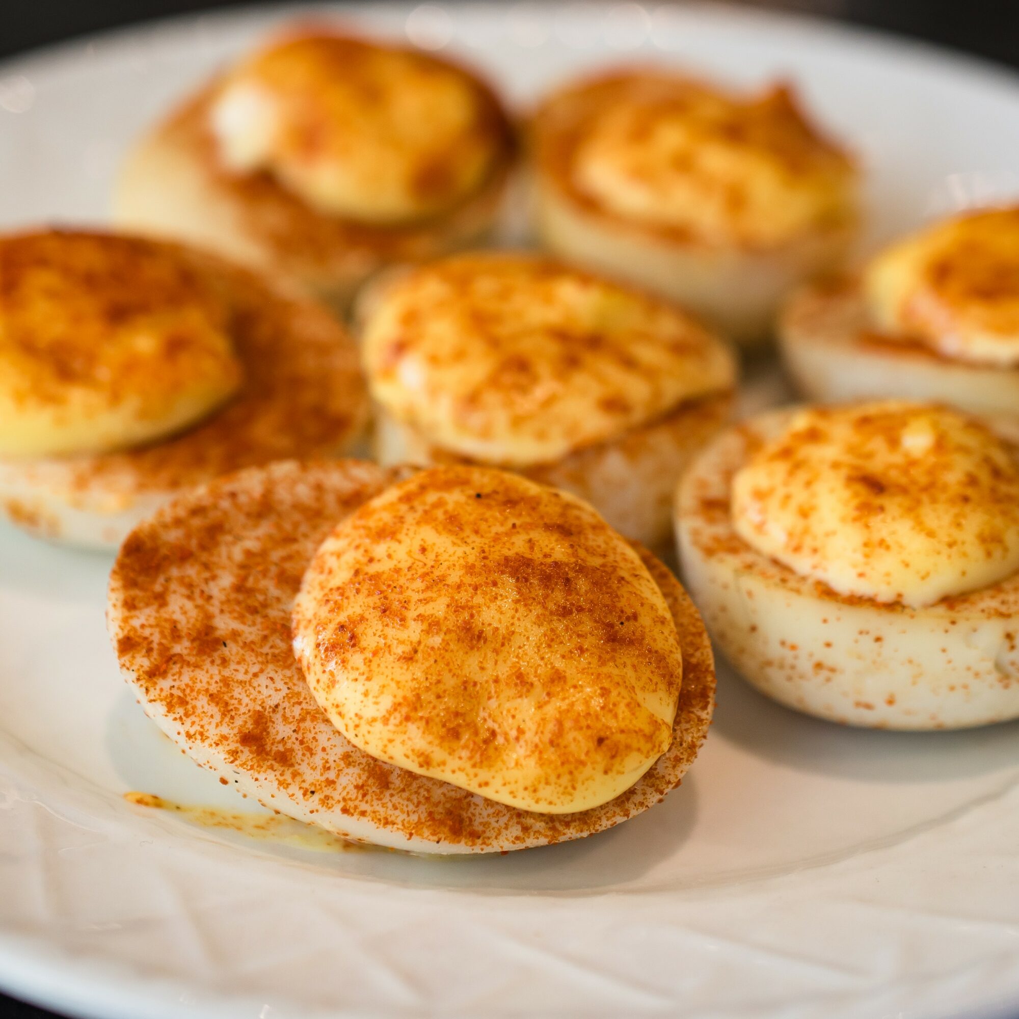 Boiled eggs topped with paprika on a white plate, some eggs are cut in half showing yolks, close-up view.