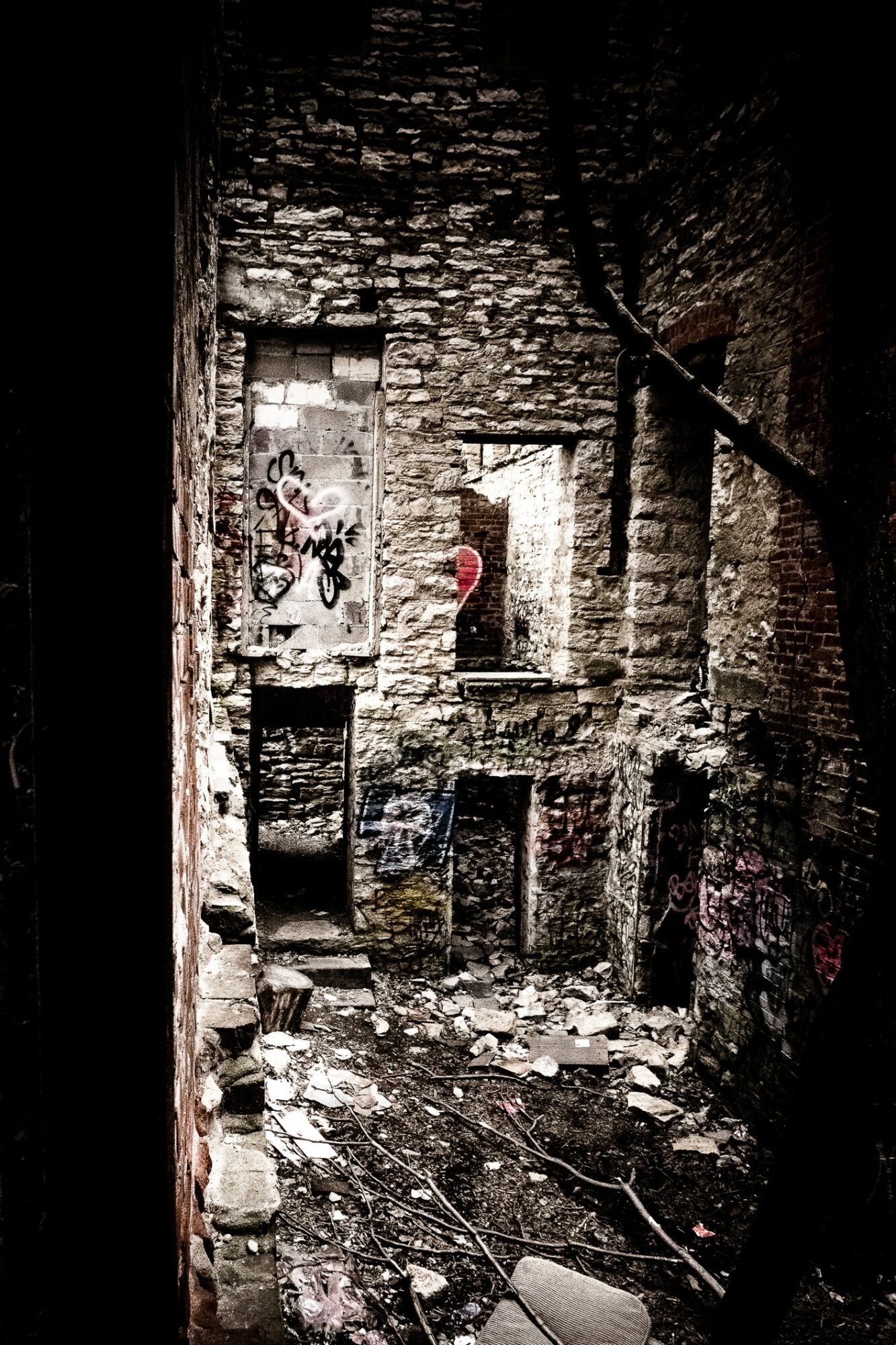 Interior of a dilapidated brick building with broken walls, debris, and graffiti, viewed from the side. Word count: 20.