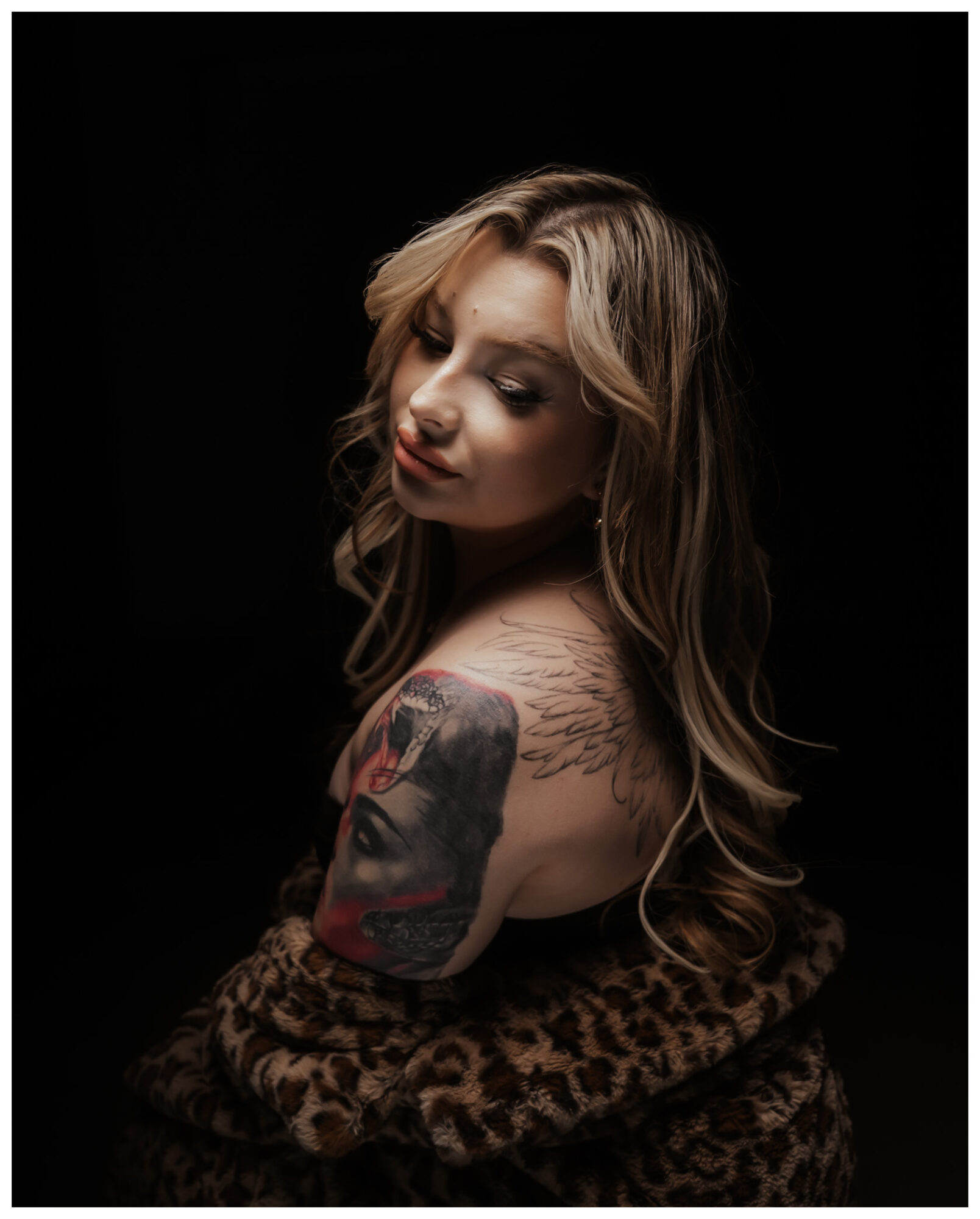 Young woman with wavy hair and a tattoo on her arm, looking over her shoulder, wrapped in a leopard print fabric.
