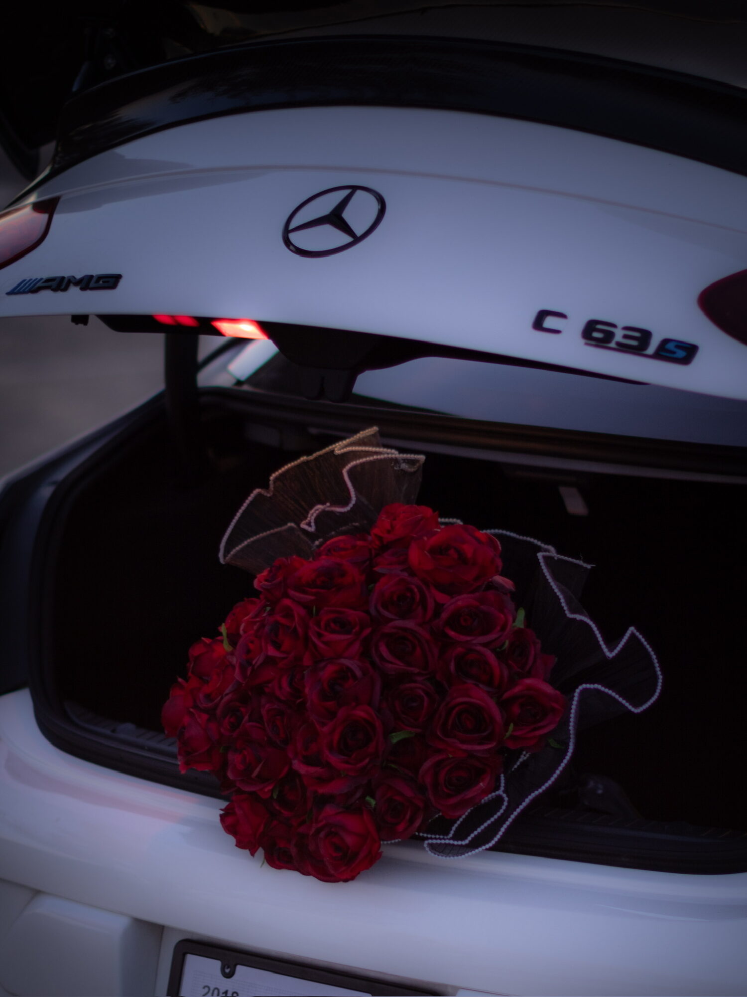 Open car trunk with a bouquet of red roses inside, Mercedes-Benz C 63 S logo visible on the car.