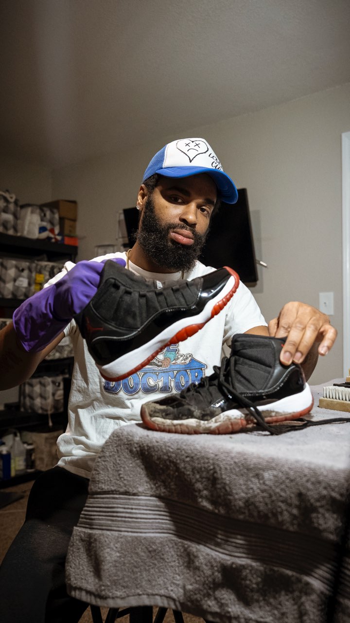 Person with beard wearing a white cap, purple gloves, and a white shirt, handling shoes on a table.