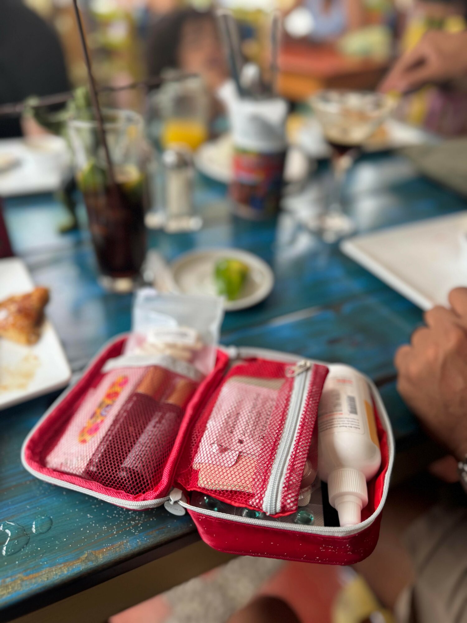 Red first aid kit open on table with bandages and medical supplies, surrounded by drinks and food at a social gathering.