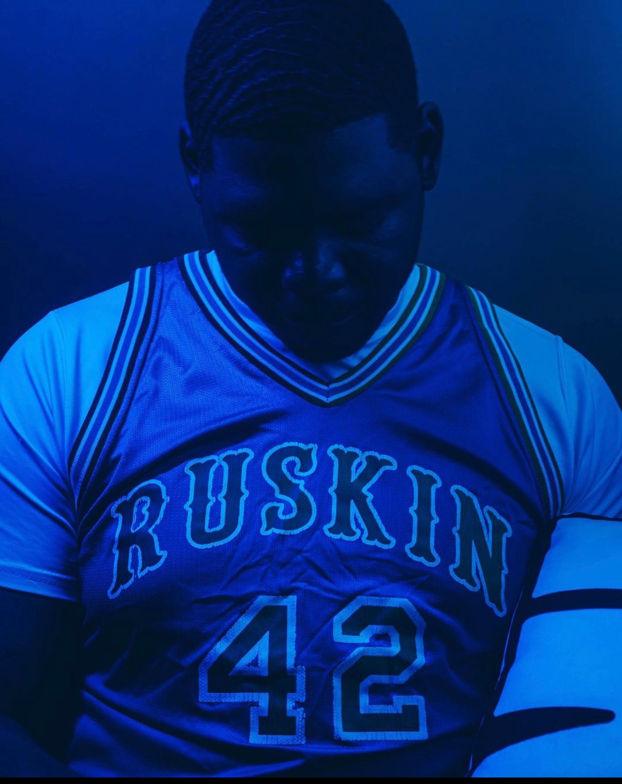 Person wearing a sports jersey with the word 'RUSKIN' and the number 42, dark lighting, facing downward.