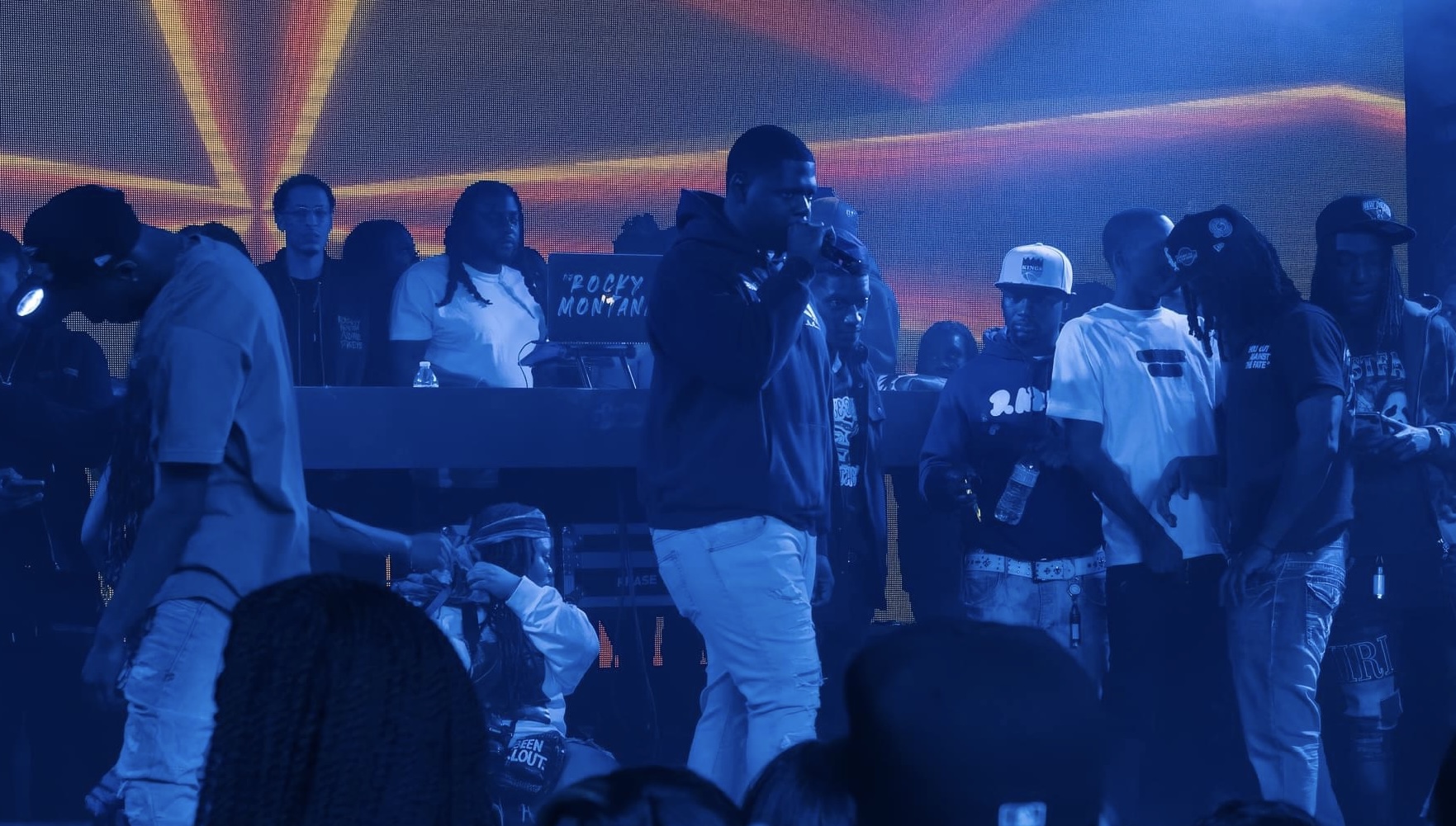 Group of people in a nightclub with colorful lights, some dancing and socializing, dark atmosphere, blue lighting, crowded scene.
