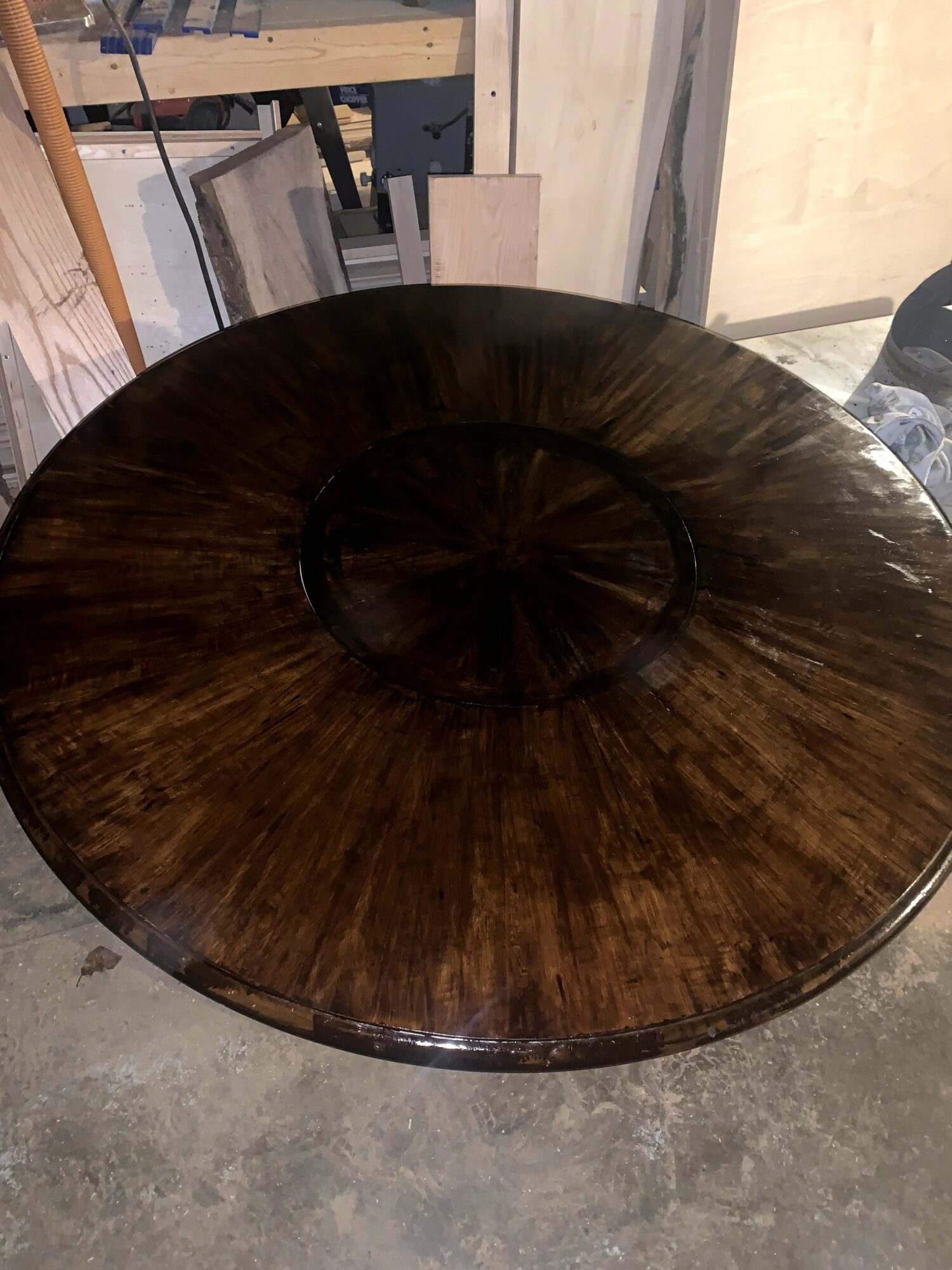 Round wooden table with a dark finish, placed on a concrete floor in a workshop setting.