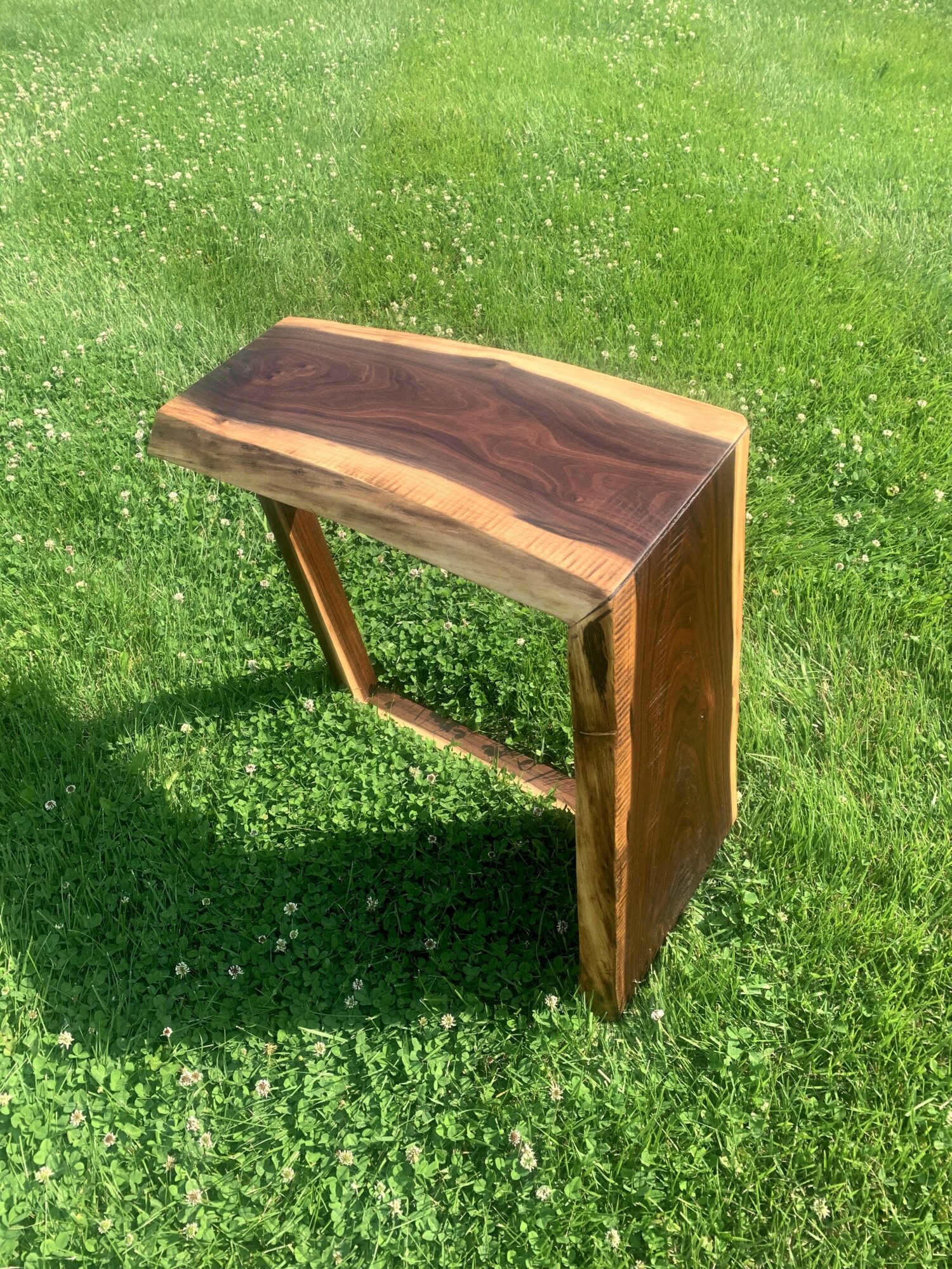 Wooden table with a natural edge, placed on green grass, casting a shadow.
