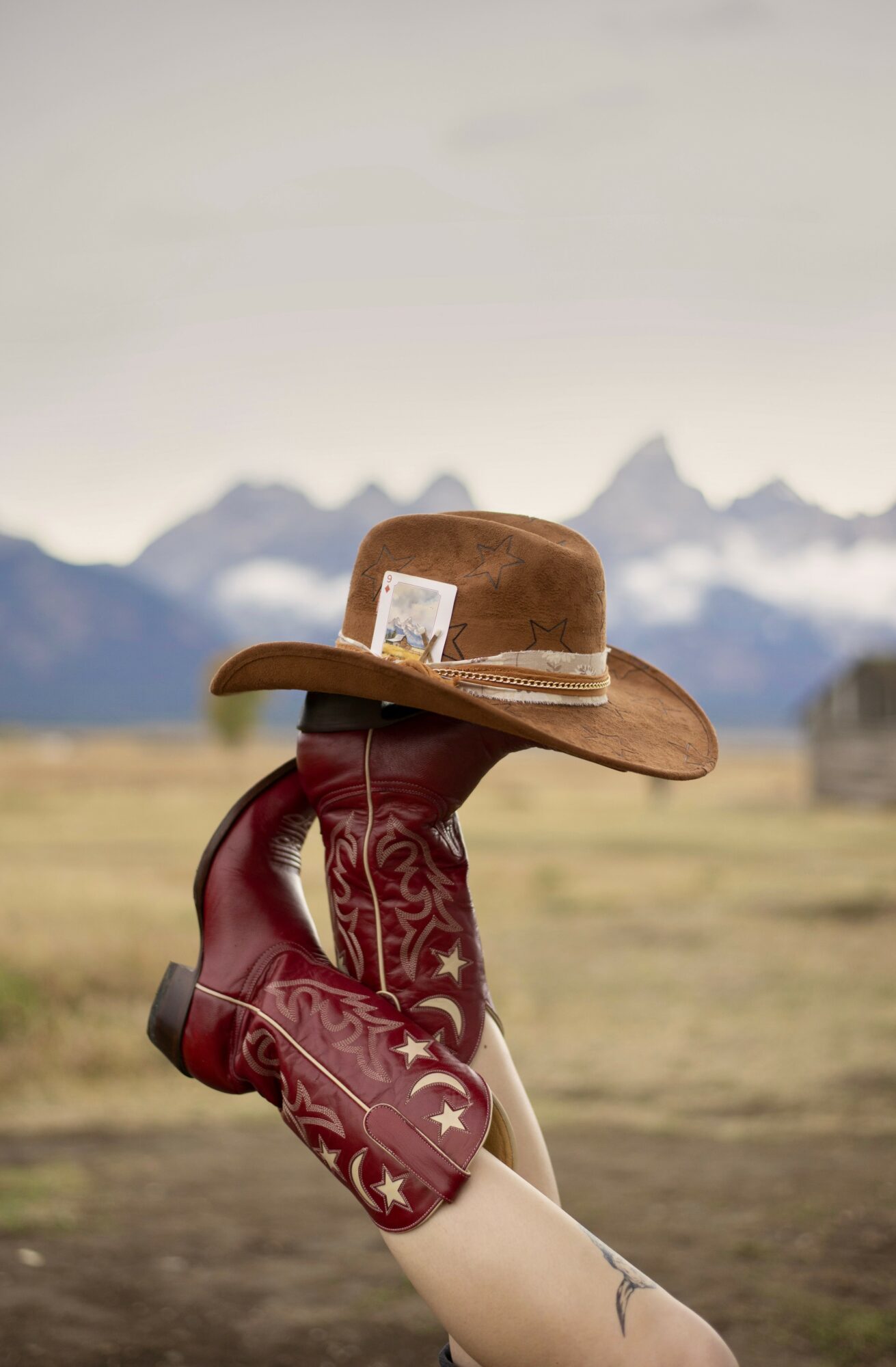 A person wearing a cowboy hat and red gloves with white star patterns, standing outdoors with mountains in the background.