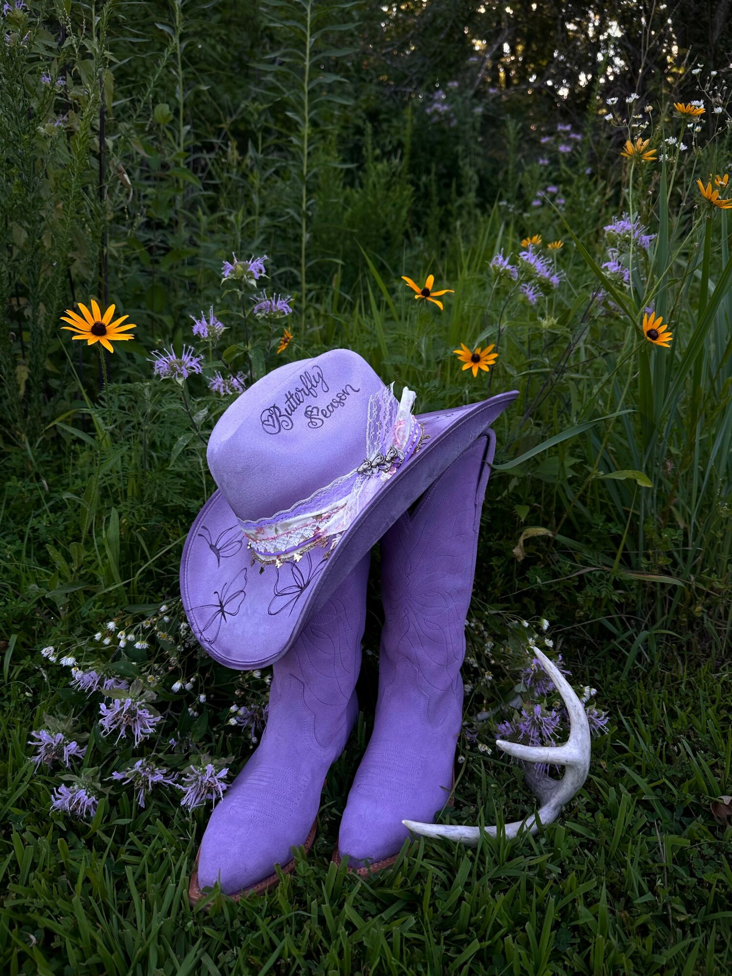 Purple boots with a white hat and a small white object, surrounded by green grass and colorful wildflowers.