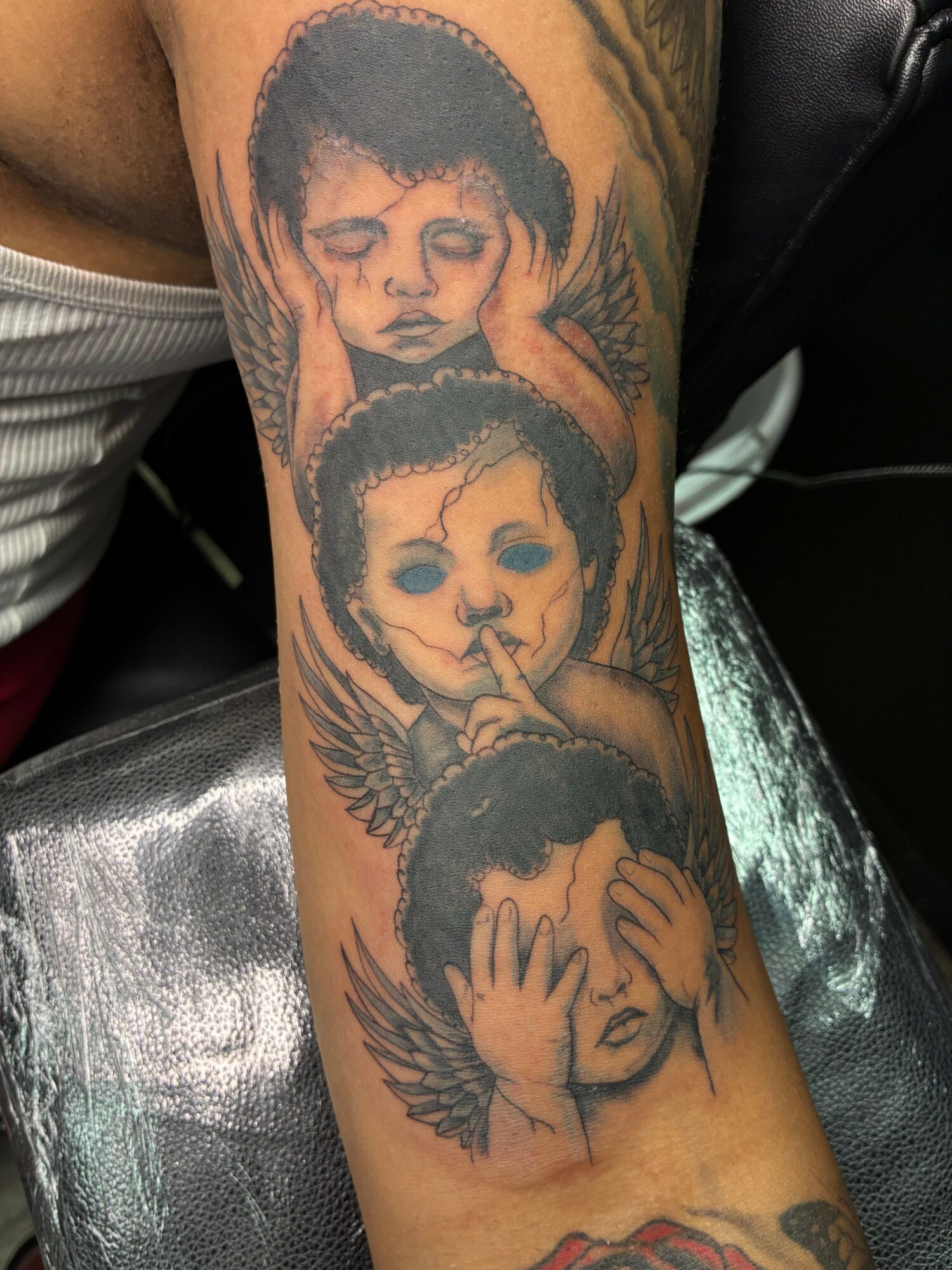 Tattoo of four children with different expressions, some with wings, on person's arm.