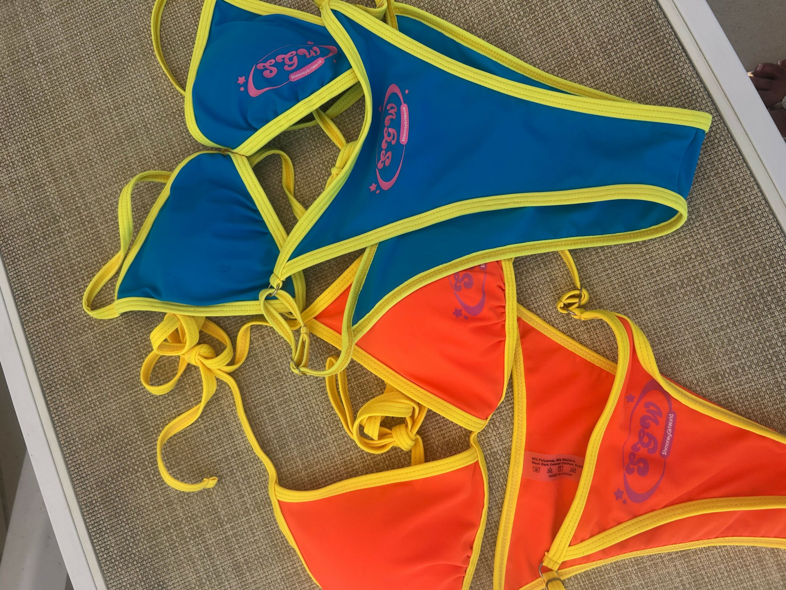 Colorful bikinis with yellow trim, blue and orange, laid on a surface, with visible text and logos.