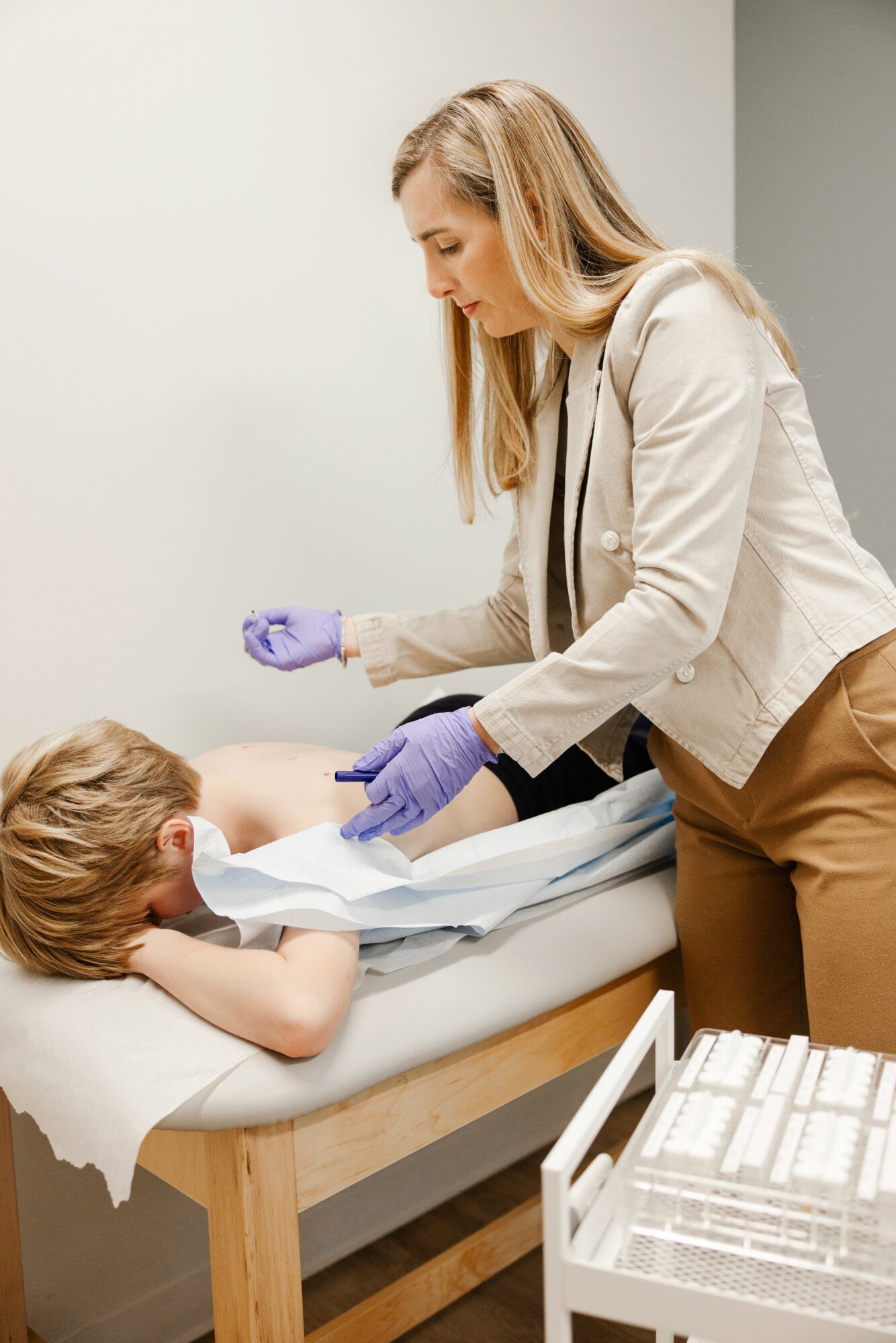 Female healthcare worker in gloves tending to a young child lying in a hospital bed, with medical supplies nearby.