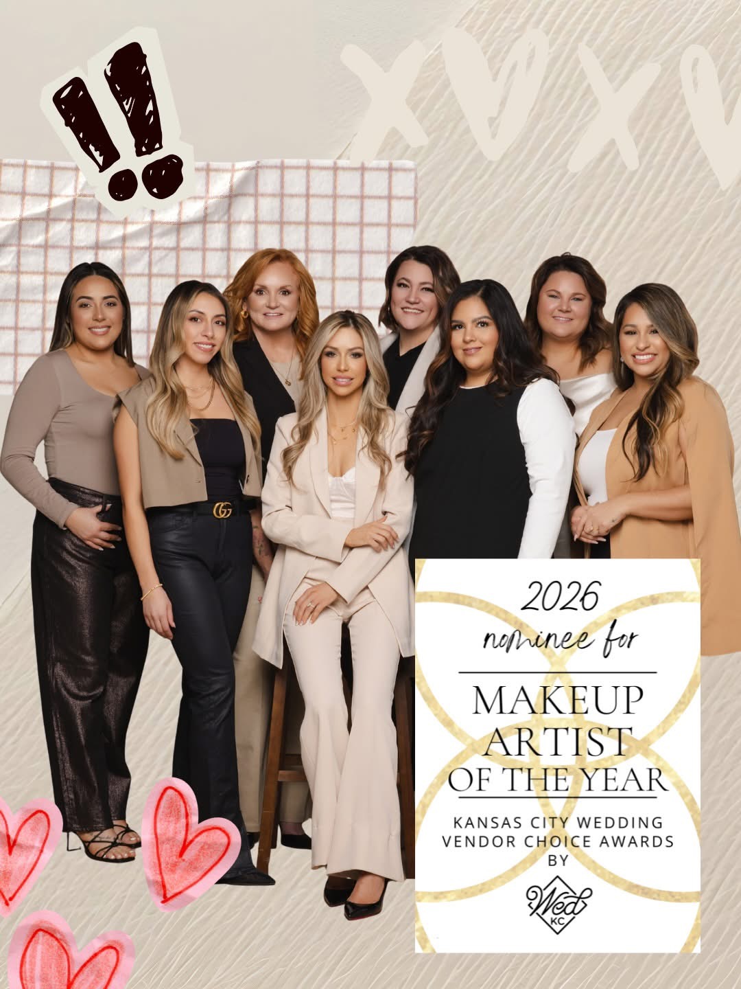 Group of eight women standing together, some smiling, in a room with decorated wall, celebrating makeup artist award, with hearts and exclamation marks.