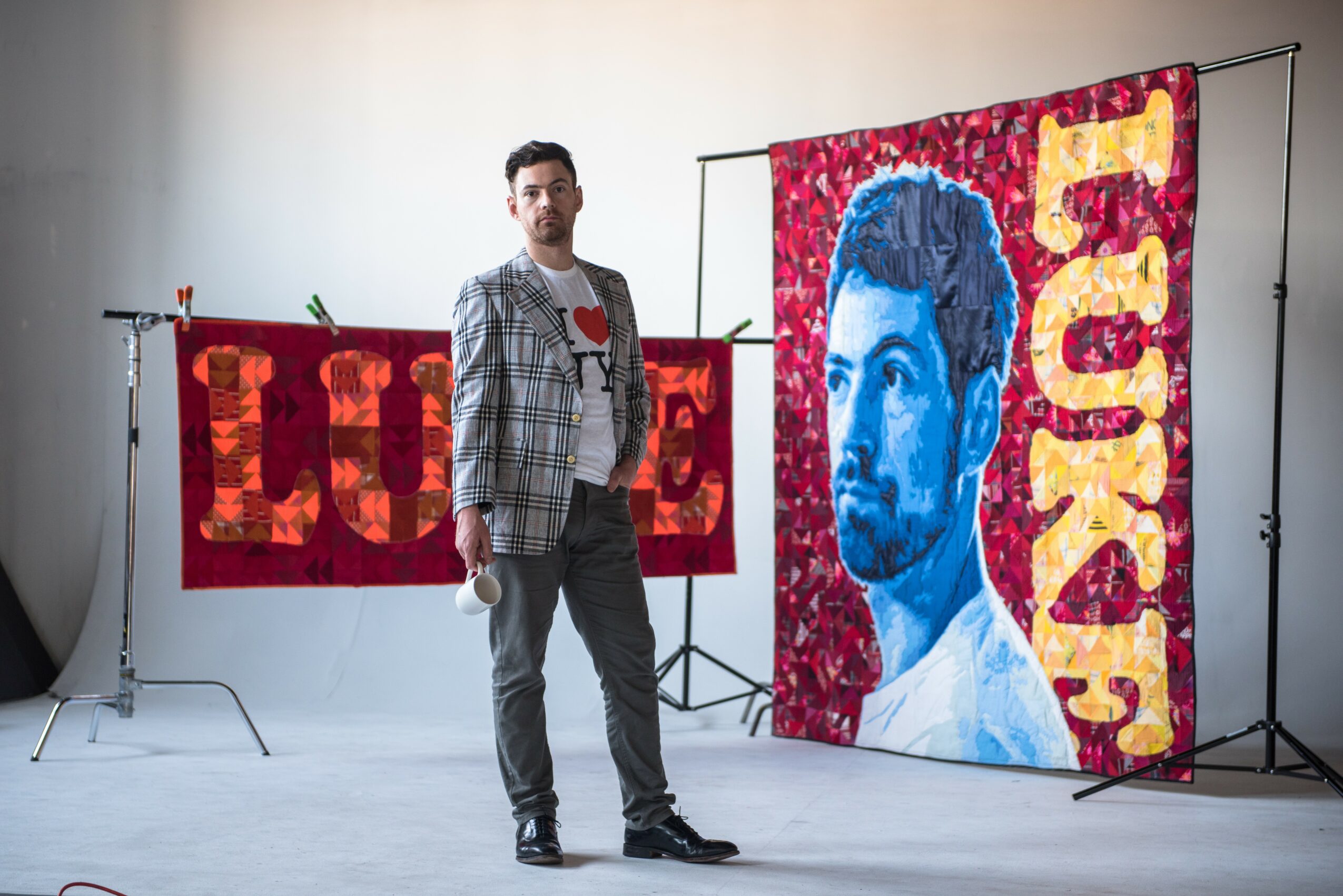 Man standing in front of colorful artwork featuring a portrait and the words 'LOVE' and 'TUCK'.