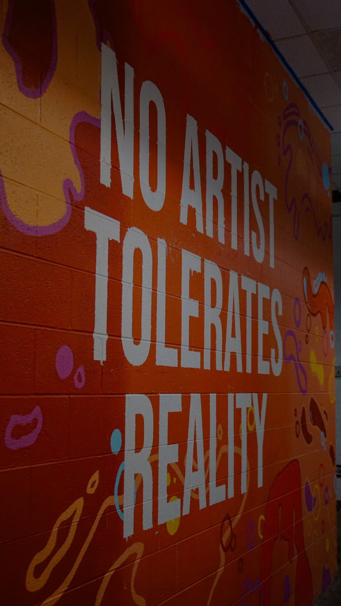 Wall with graffiti-style art and text reading 'NO ARTIST TOLERATES REALITY'.
