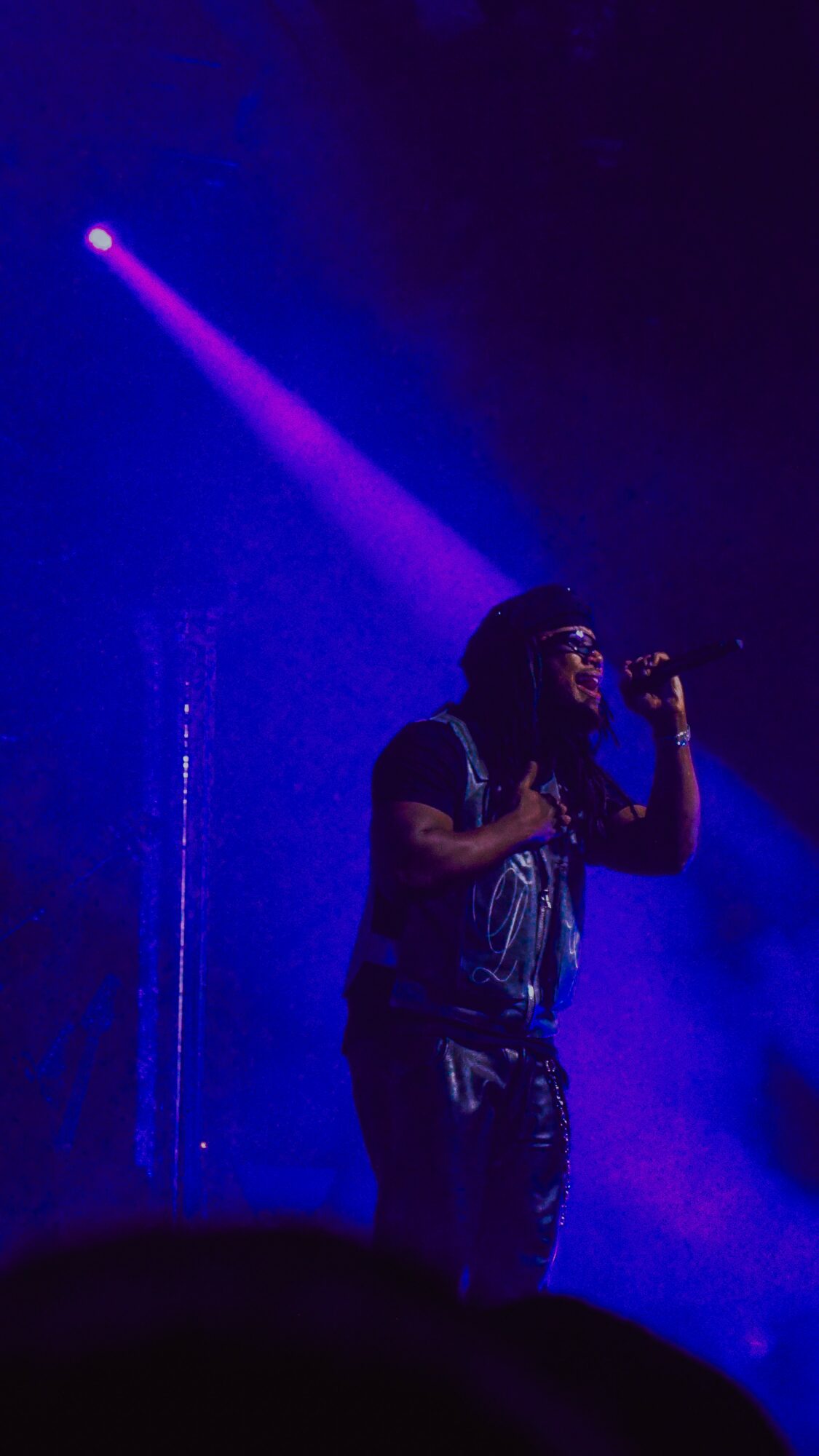 Person singing into microphone on stage with purple spotlight, dark background, and fog effects.