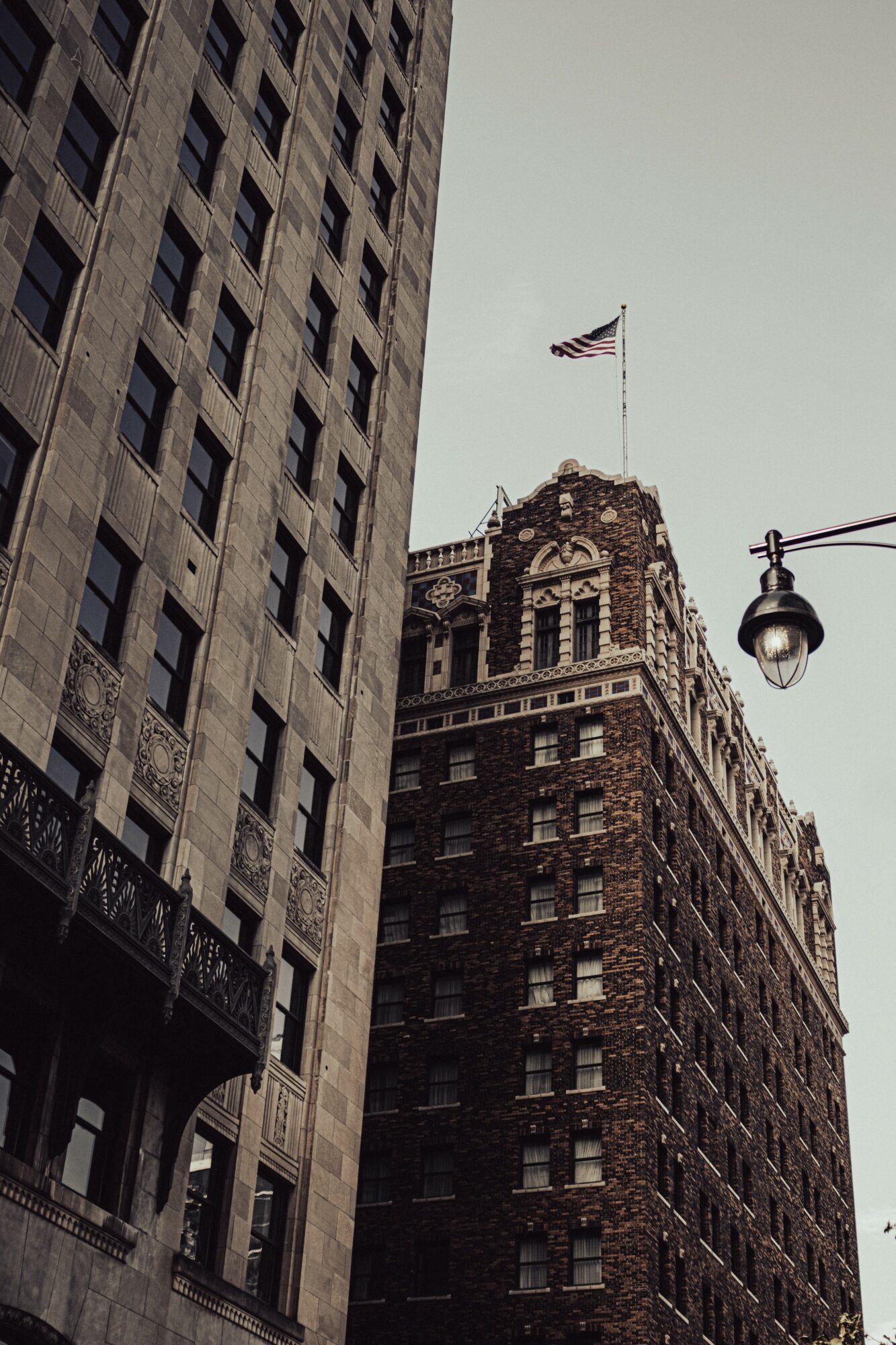 Tall building with an American flag on top, adjacent to another building, with a street lamp in foreground.