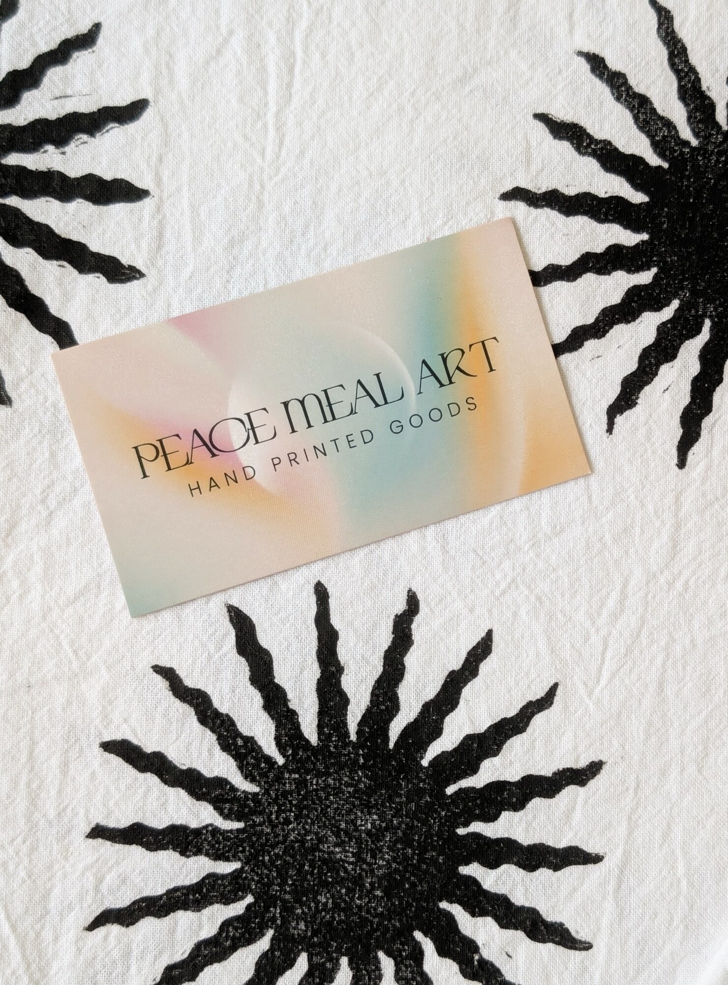Business card with pastel background and text, surrounded by black sunburst designs on white textured surface.