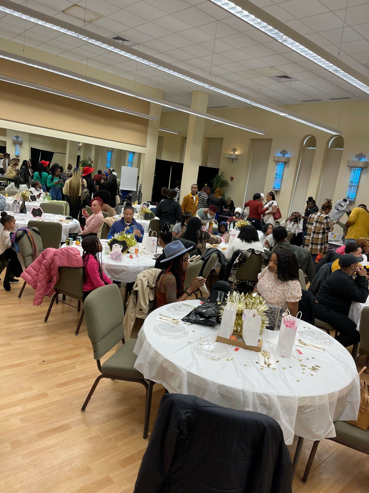 People gathered around tables in a banquet hall, some standing and some seated, with a decorated table in the foreground.