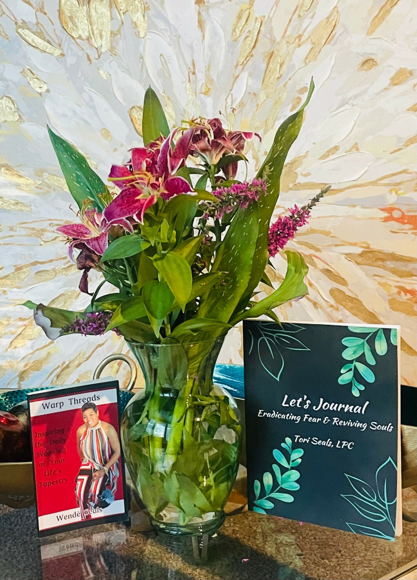 Vase with pink and purple flowers, a card, and a journal on a surface.