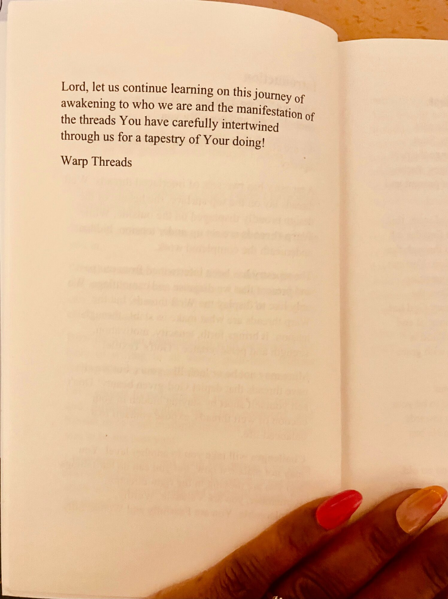 Open book with text on the left page and a person's hand with red nail polish holding the bottom right corner.