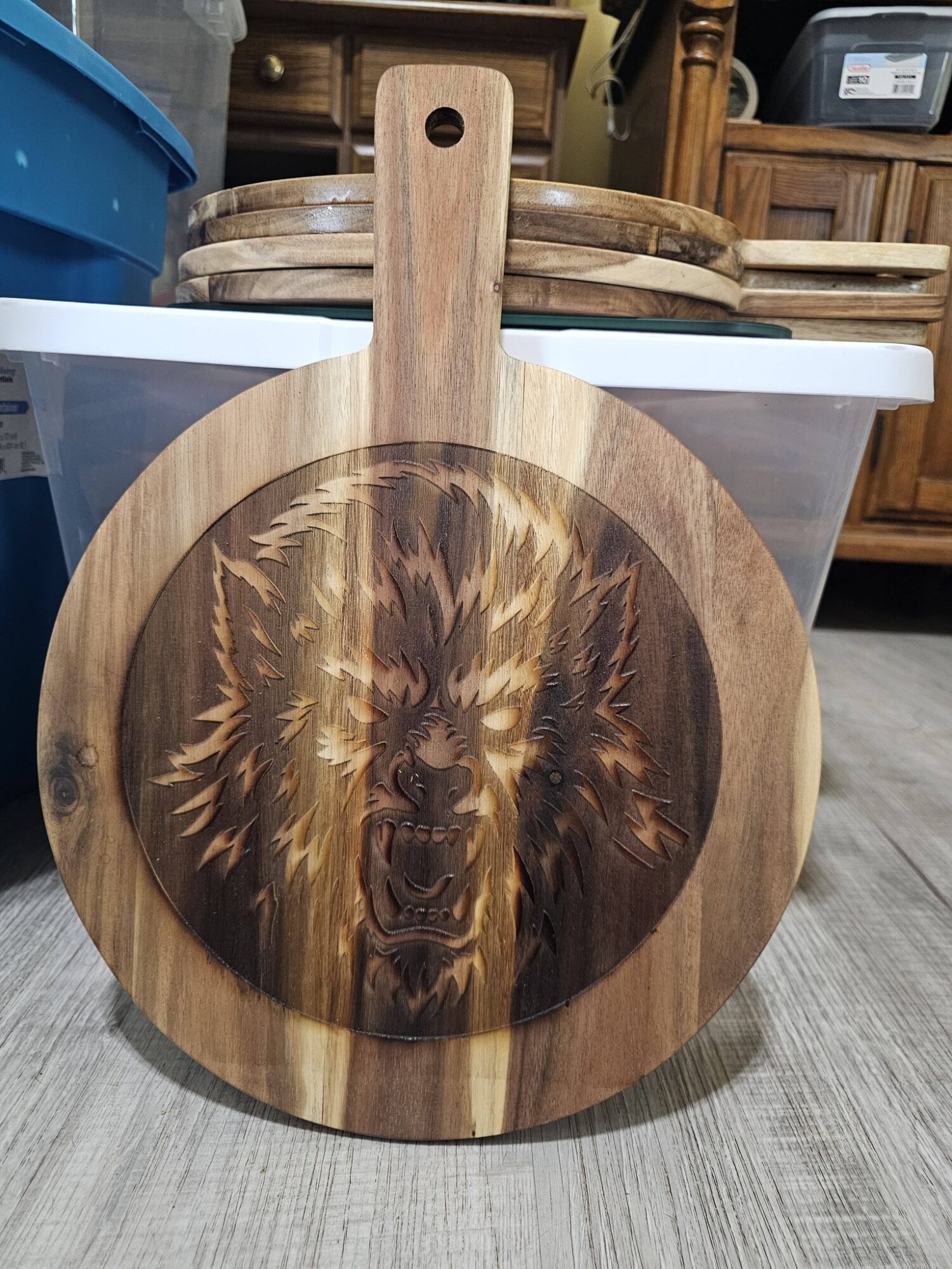 Round wooden cutting board with a lion's face engraved in the center, placed on a wooden floor.