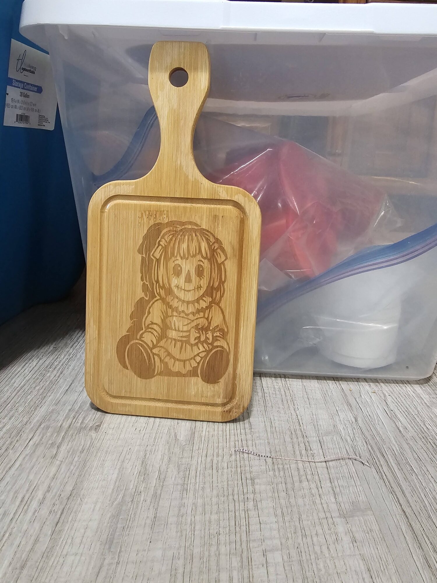 Wooden cutting board with a carved cartoon girl holding a teddy bear, placed on a wooden surface.