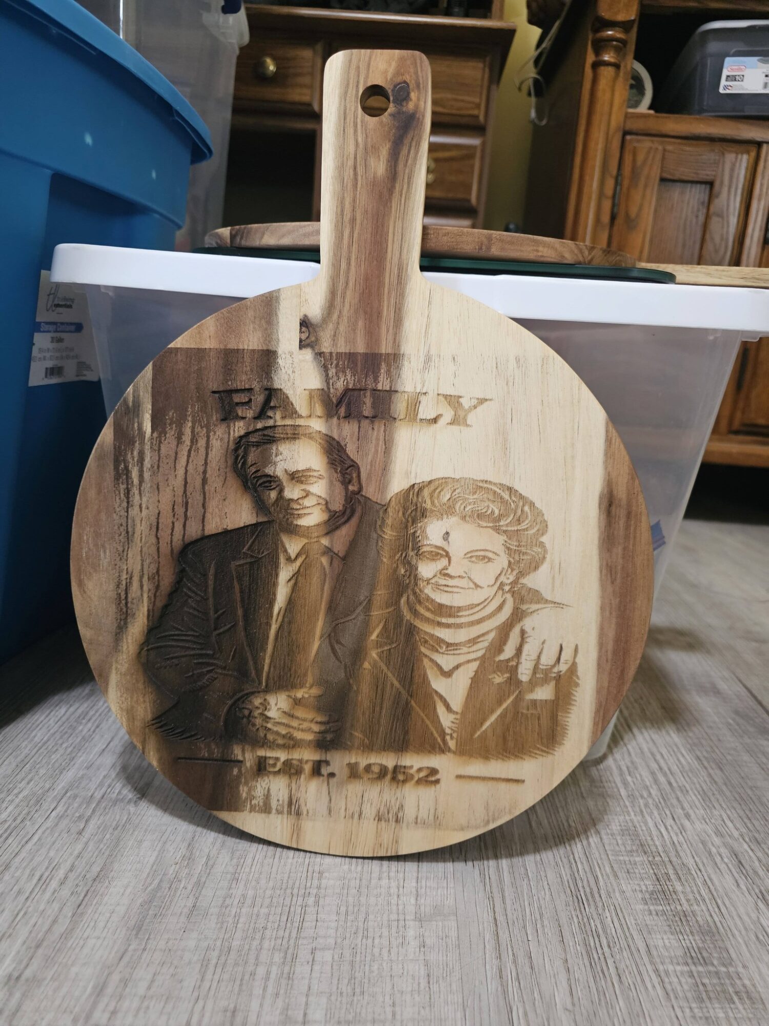 Round wooden cutting board with engraved photo of a man and woman, and text including 'Family' and 'Est. 1962'.