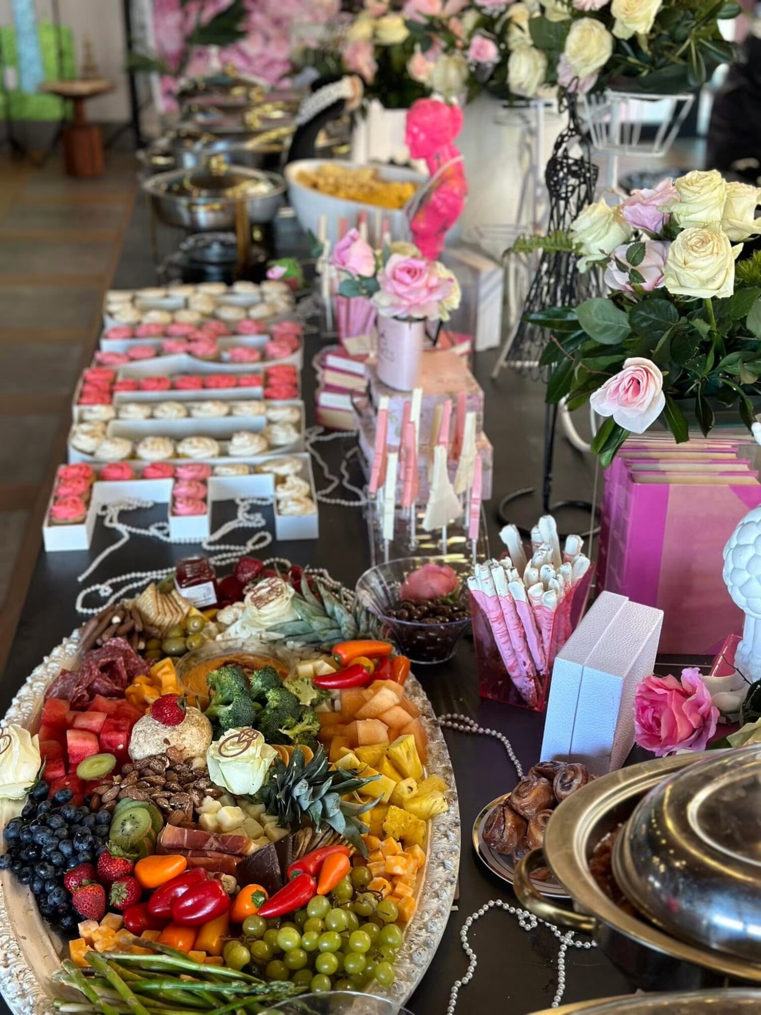 Table with colorful candies, desserts, and floral arrangements, decorated with pink and white flowers, in a festive setting.