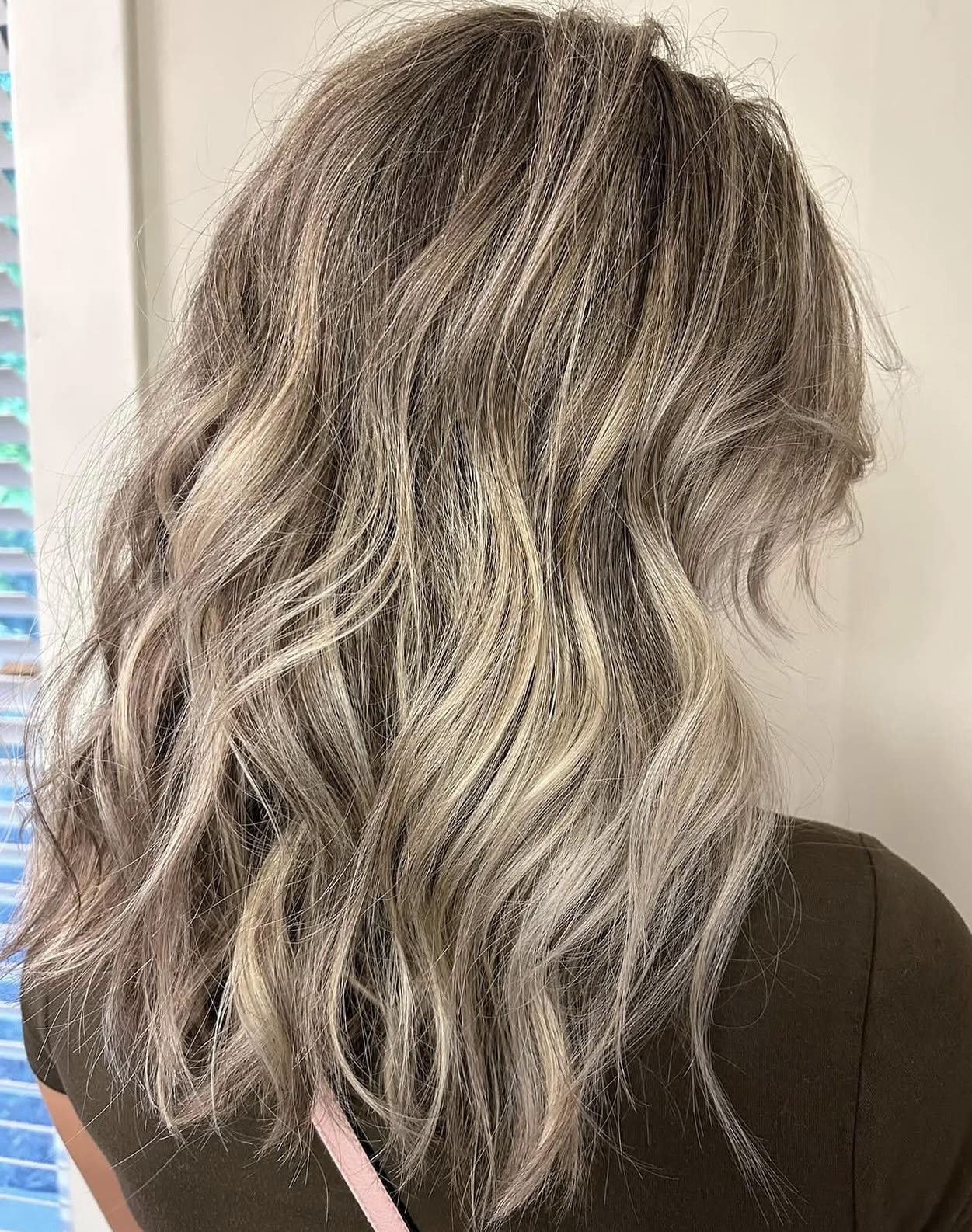 Wavy, shoulder-length hair with blonde highlights and darker roots, viewed from the back.