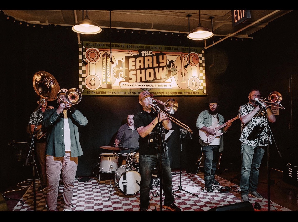 Band performing on stage with five musicians, instruments, and a banner reading 'The Early Show'.