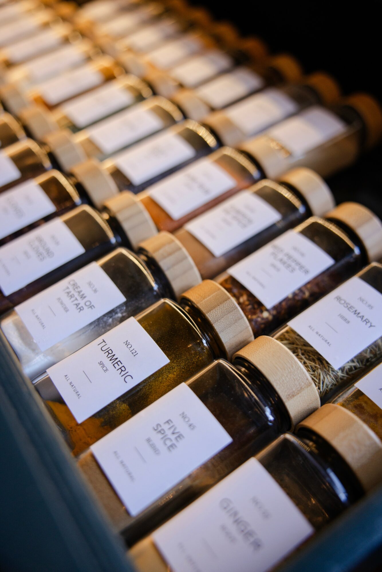 Rows of glass jars with white labels and gold lids, arranged on a shelf.