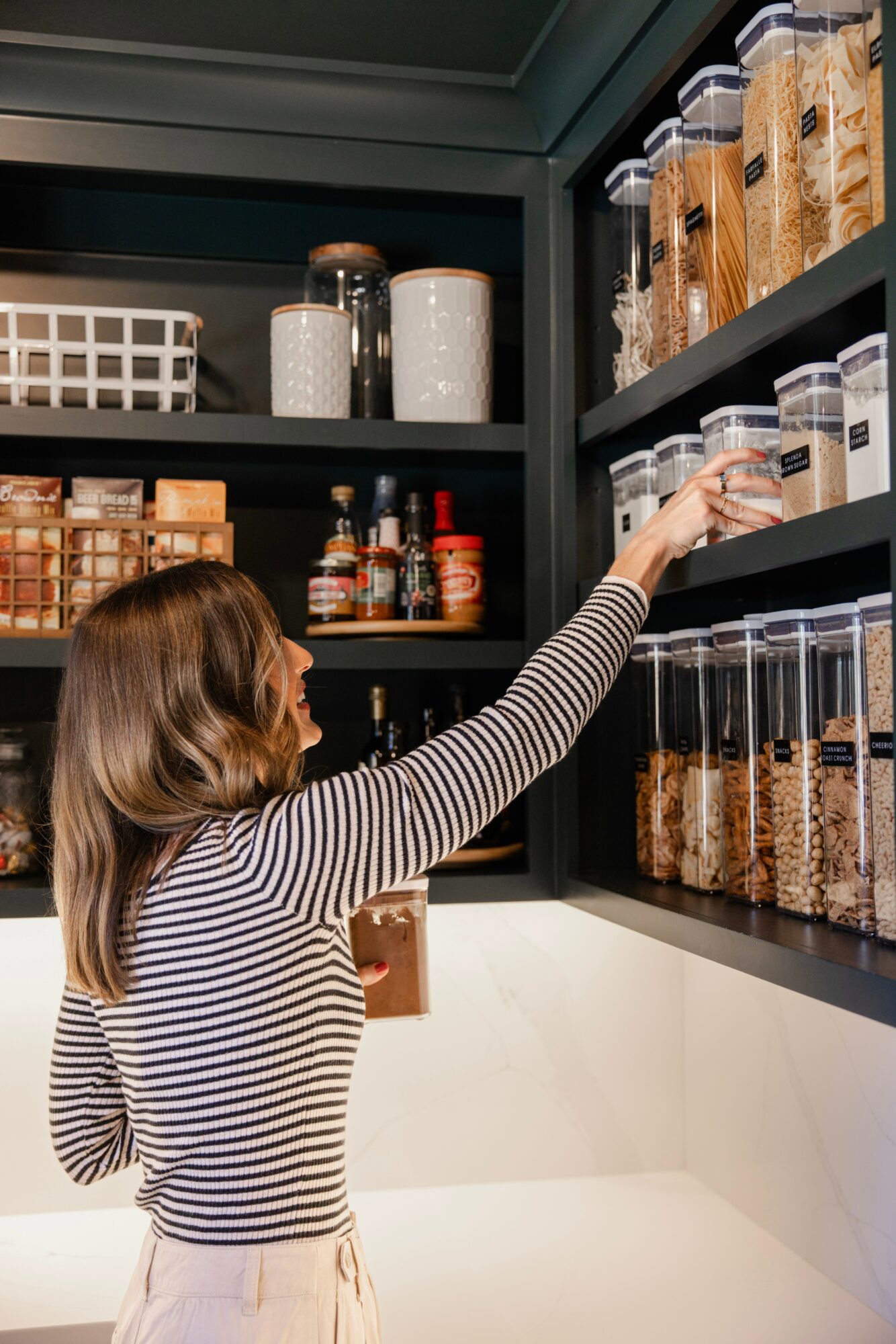 Child reaching for a jar on a pantry shelf filled with containers and food items.