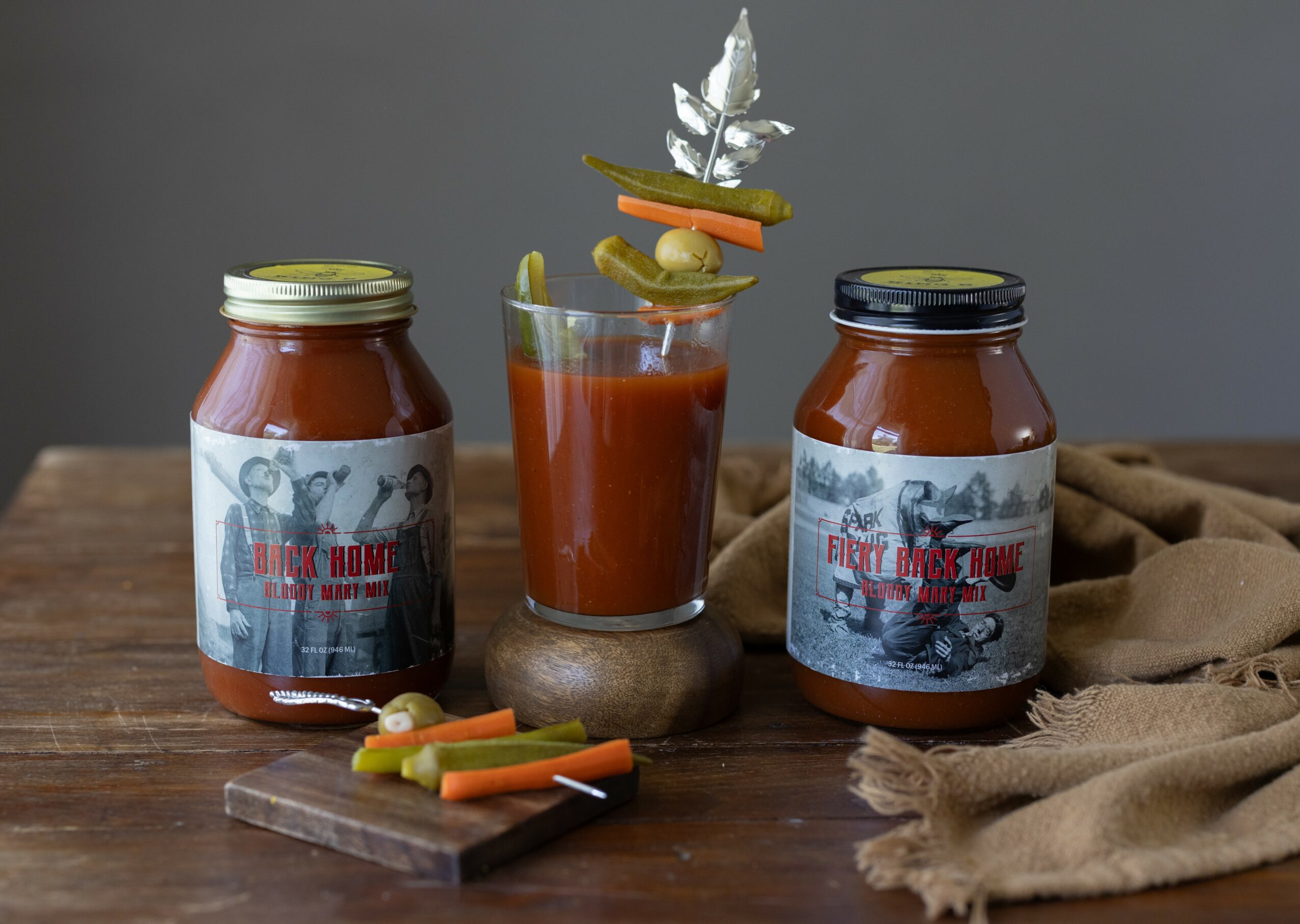 Two jars of sauce and a glass with vegetable sticks on a wooden surface, with a cloth nearby.