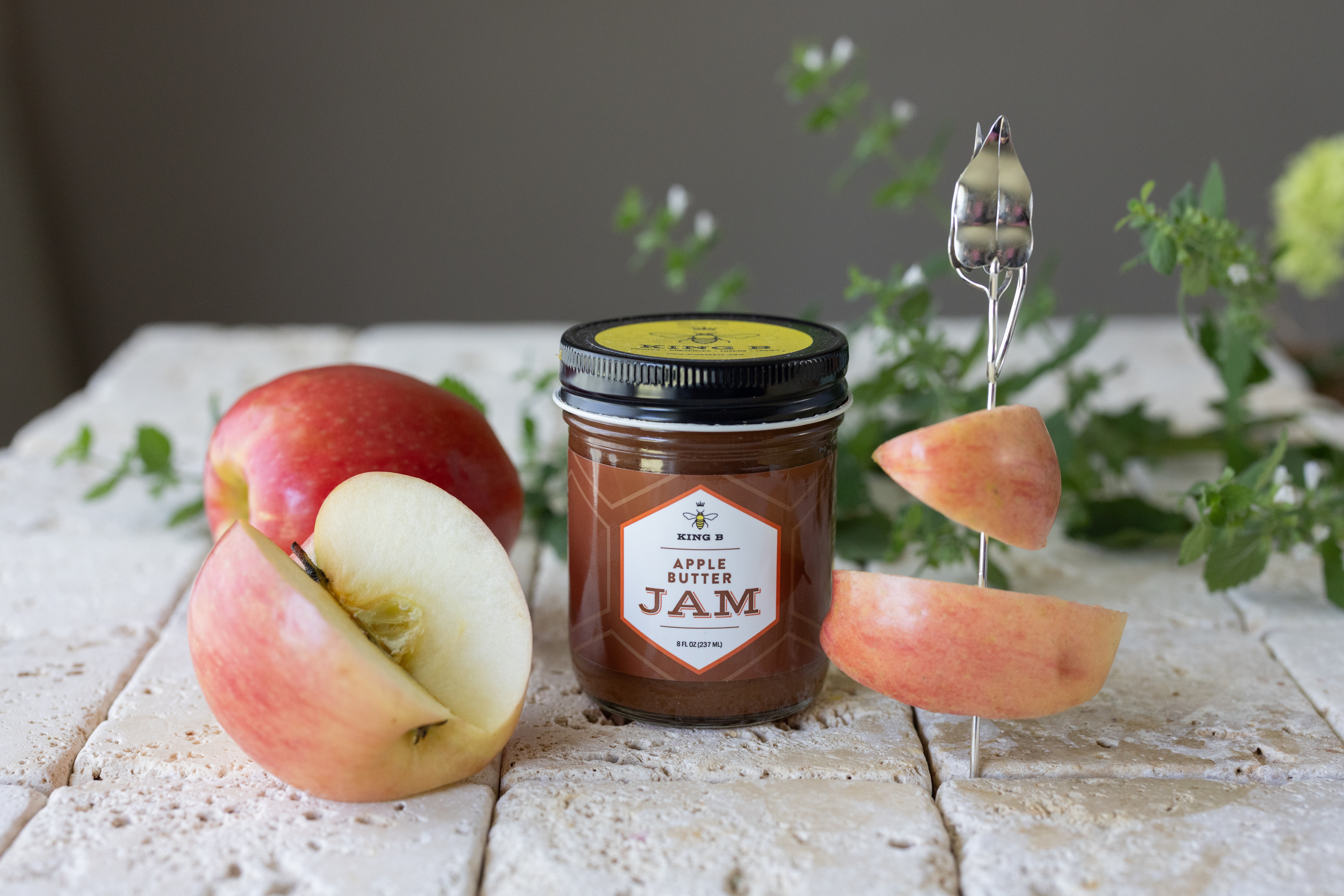 A jar of jam, a partially eaten apple, and a skewer with apple slices on a rustic wooden surface.