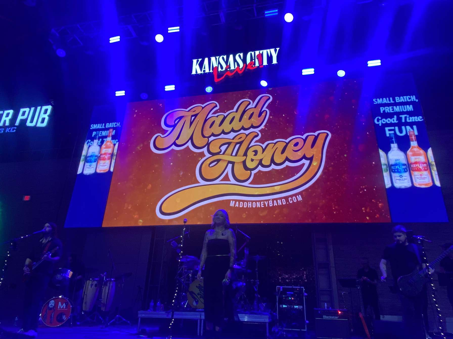 Stage with large screen displaying 'Madd Honey' logo, 'Kansas City' above, and band setup with instruments below.