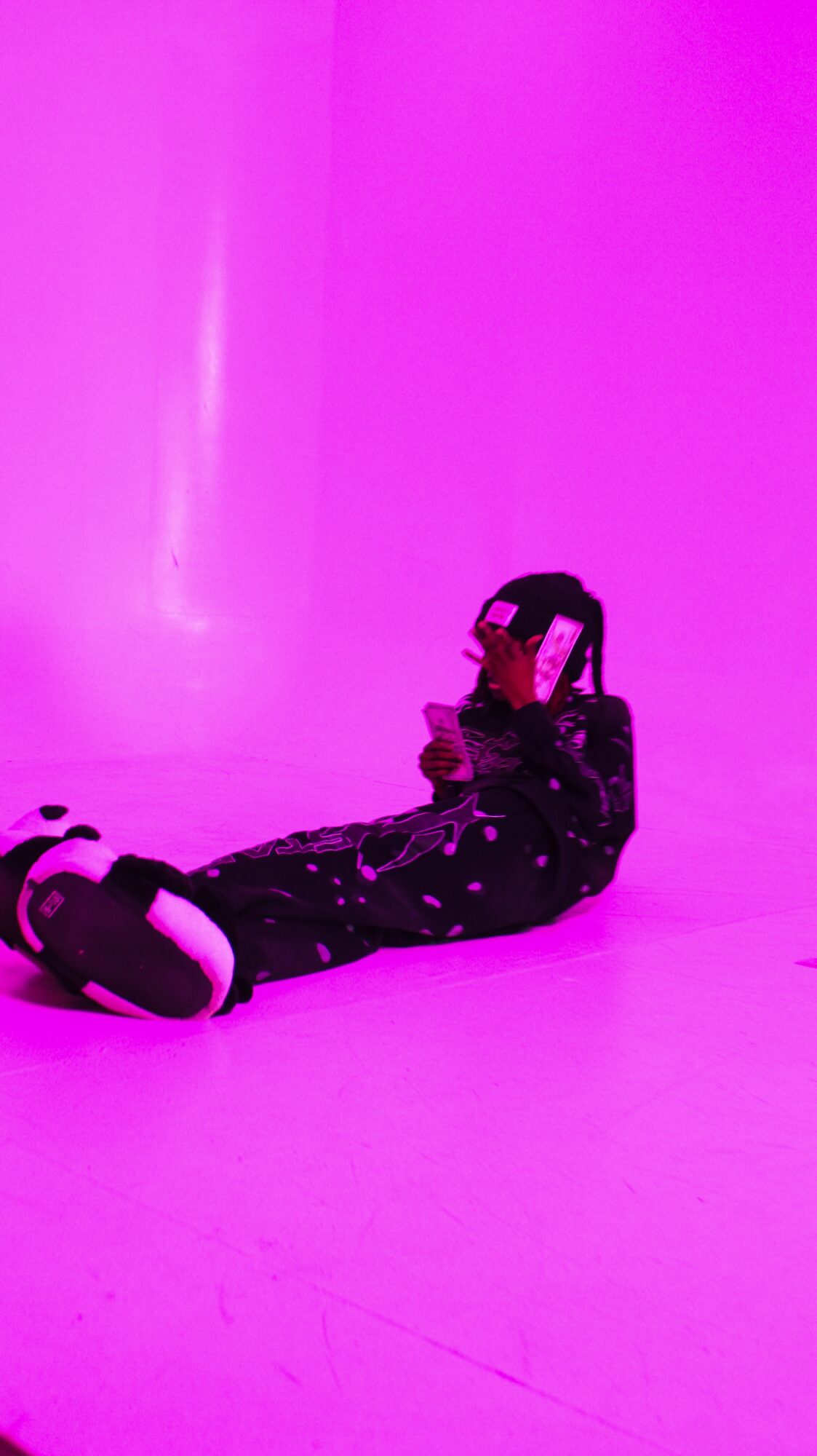 Person lying on the floor holding a virtual reality headset, illuminated by pink and purple lighting.