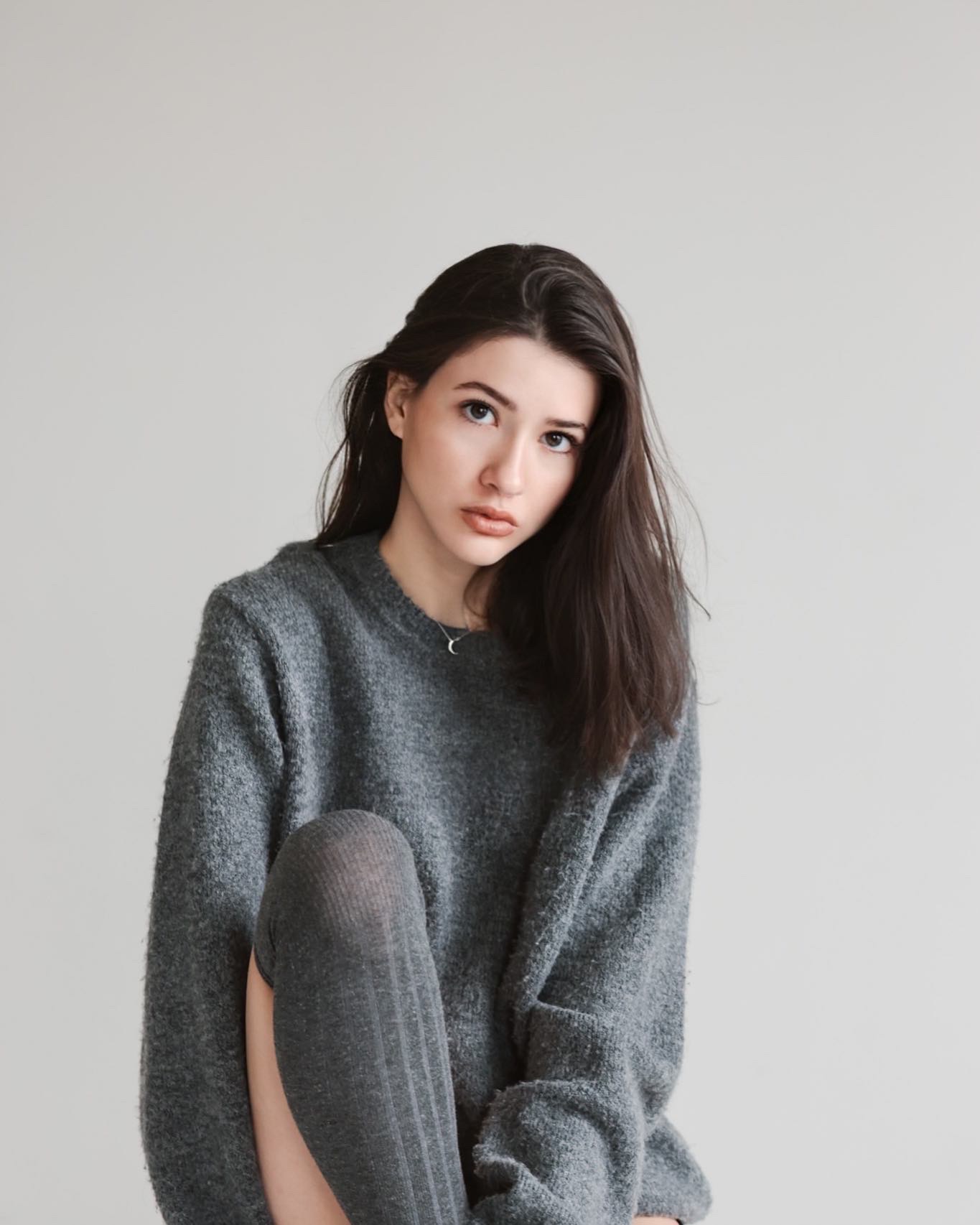 Young woman with long dark hair wearing a gray sweater, looking at the camera against a plain background.