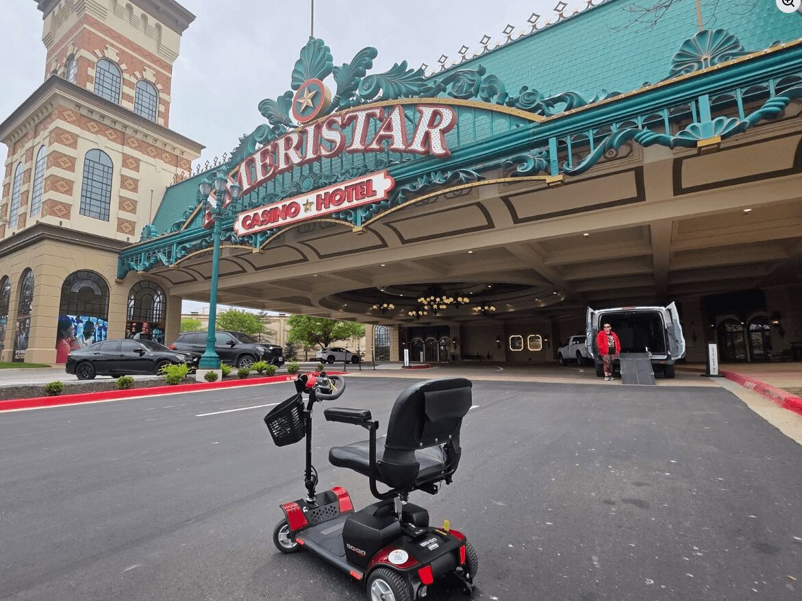 Casino entrance with a teal awning and decorative elements, people walking nearby, and a building with a tower in the background.