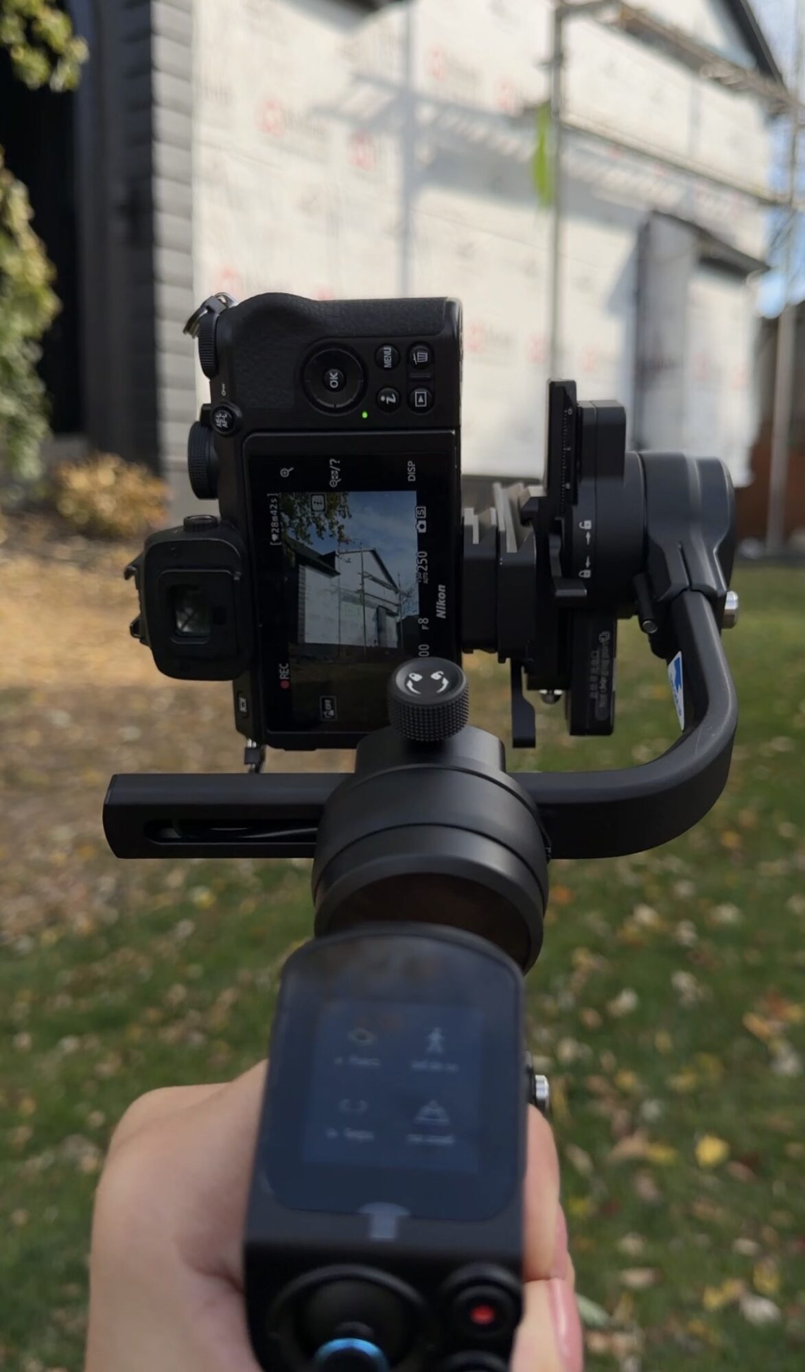 Camera mounted on a stabilizer outdoors with a blurred background of buildings and trees.