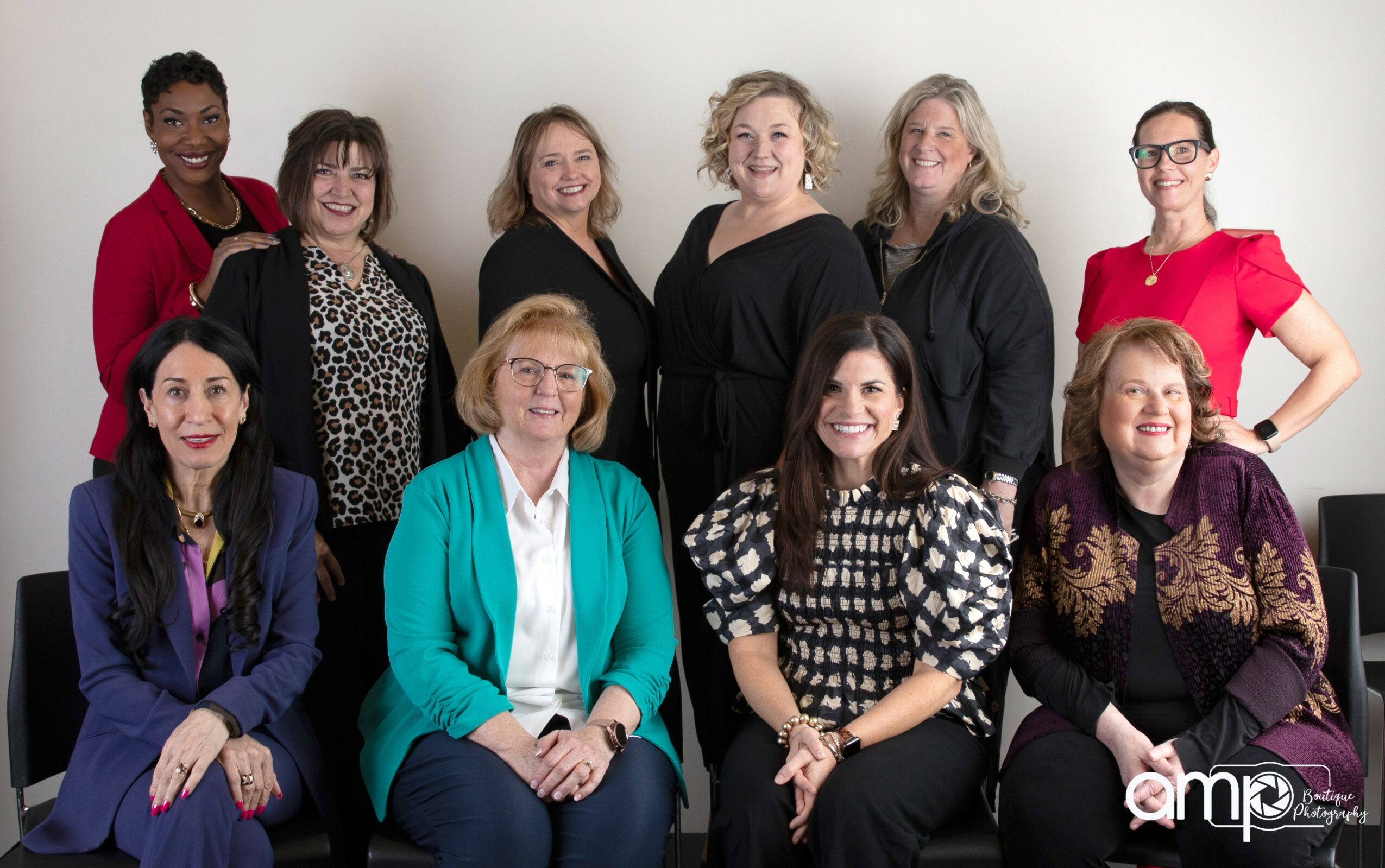 Group of ten women posing together indoors, some standing and some sitting, smiling at the camera.