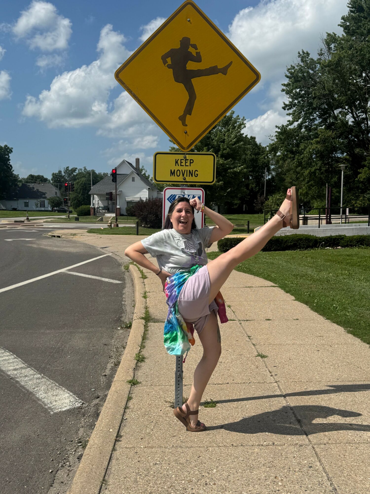 Person performing a dance or gymnastic move on sidewalk, with a yellow pedestrian crossing sign and blue sky in background.