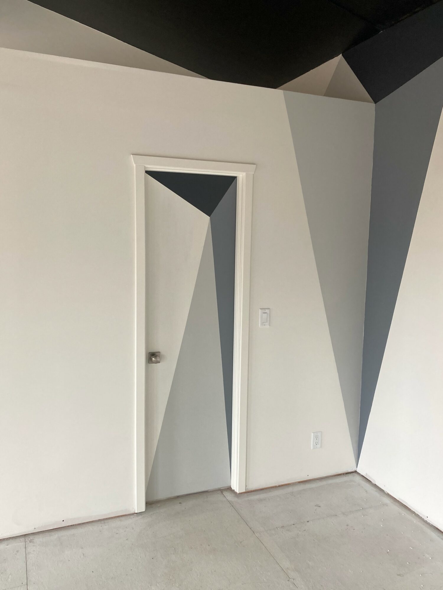 Doorway with geometric shadows and angled ceiling, white walls, and a gray floor.